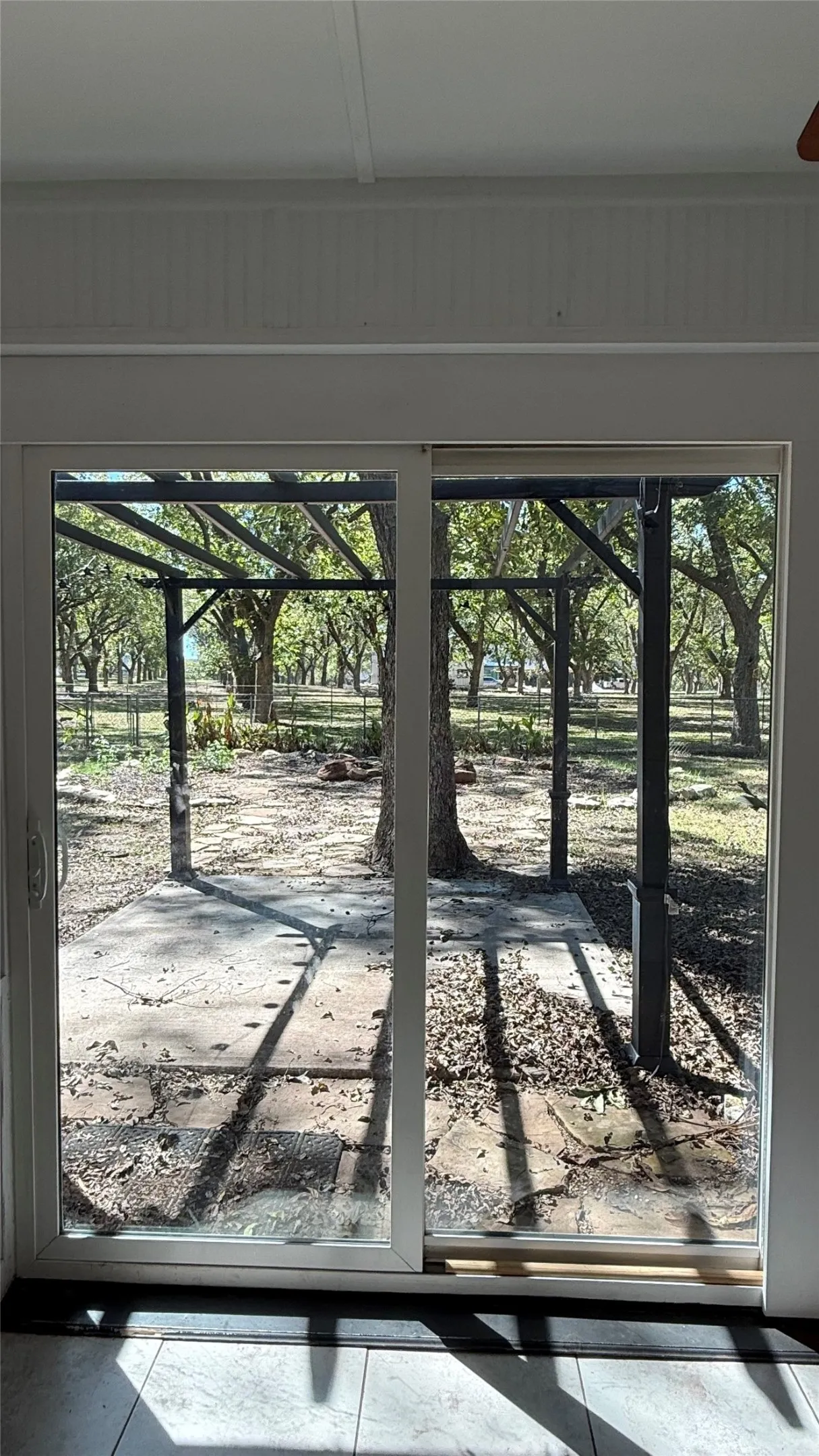 Sliding glass patio door with a concrete patio and a metal pergola, surrounded by mature trees. This is set up to be a dream backyard.