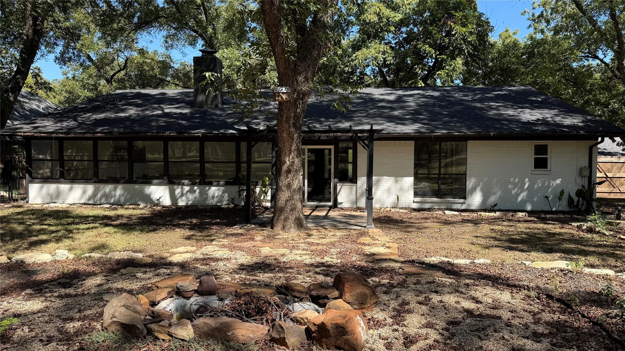 Rear exterior featuring a sunroom with multiple windows, a prominent chimney, and a stone-lined fire pit area
