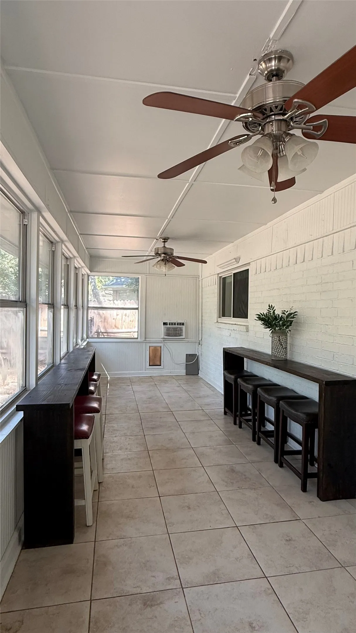 Enclosed sunroom featuring tile flooring, multiple ceiling fans with integrated lighting, and extensive wall of windows overlooking the peaceful backyard. Also has a doggy door that leads to it's own secured area.