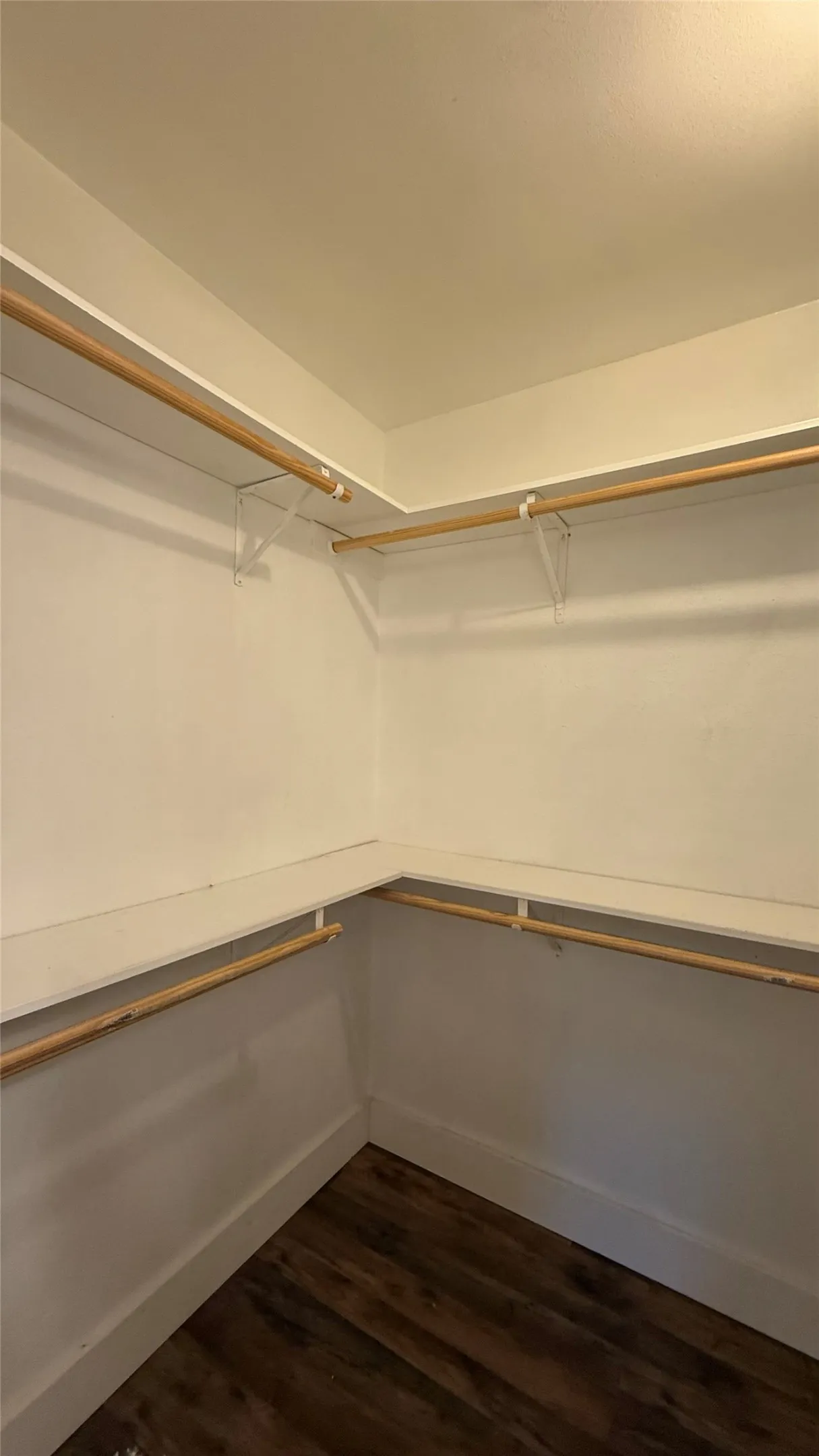 Wood-finish flooring with white walls and built-in closet shelving and hanging rods