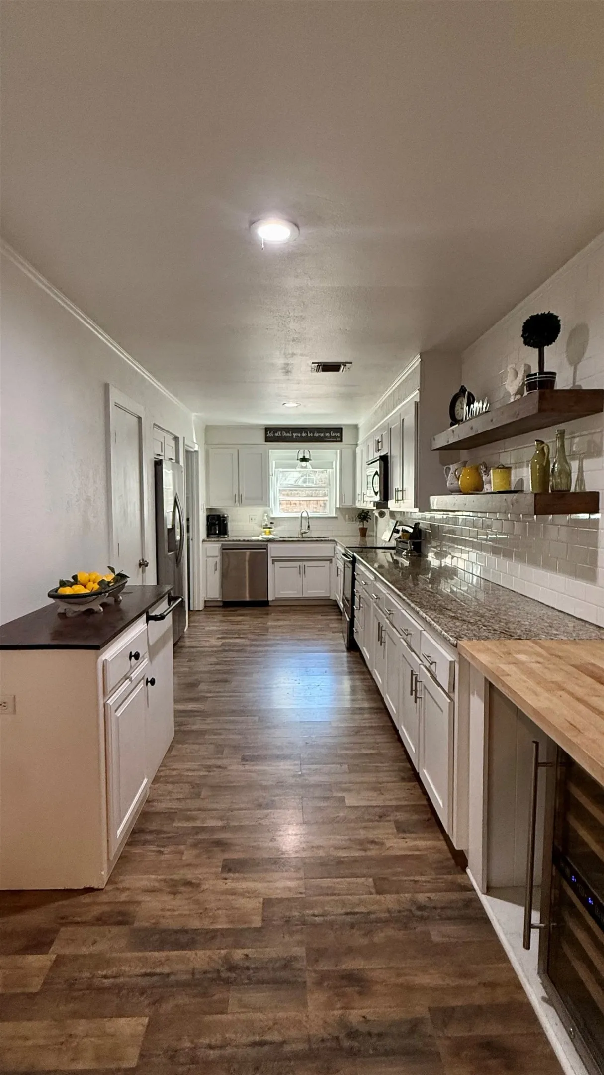 Galley kitchen featuring wood-finish flooring, white cabinetry, granite-style countertops, stainless steel appliances, and a tile backsplash