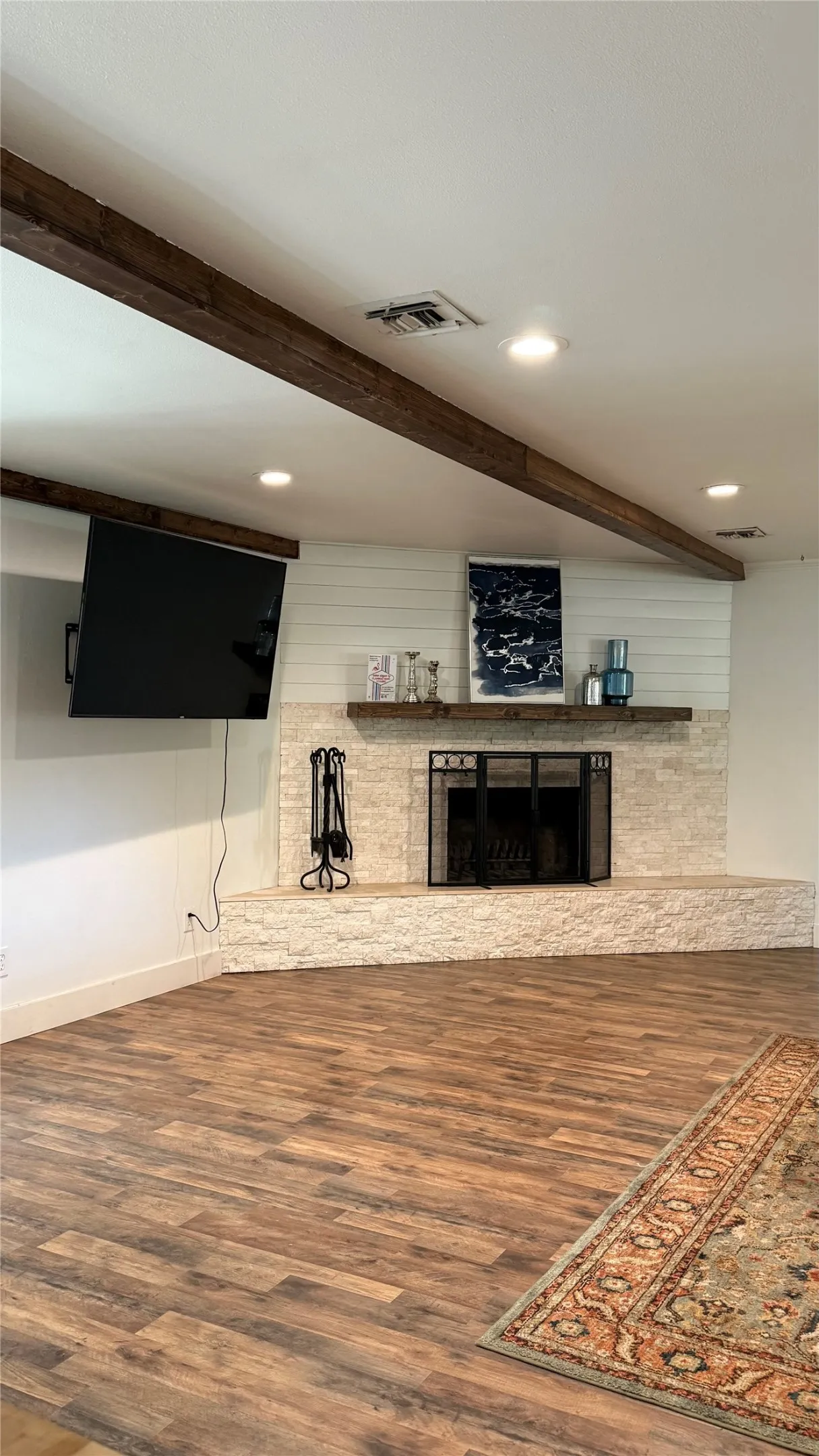 Exposed wood beams, recessed lighting, wood-finish flooring, stone-clad fireplace with mantel, and shiplap accent wall