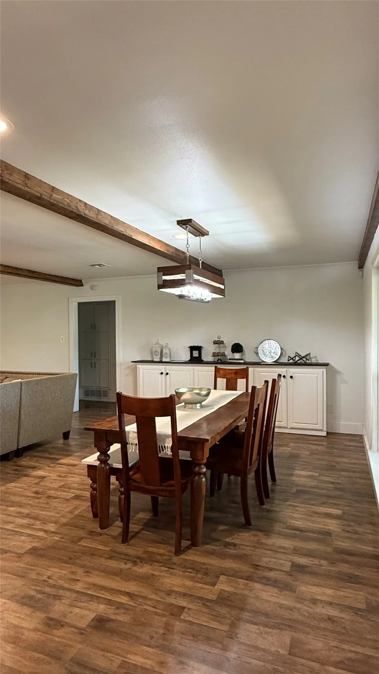 Wood-finish flooring, exposed ceiling beams, built-in lower cabinetry, dark countertop, and a contemporary chandelier
