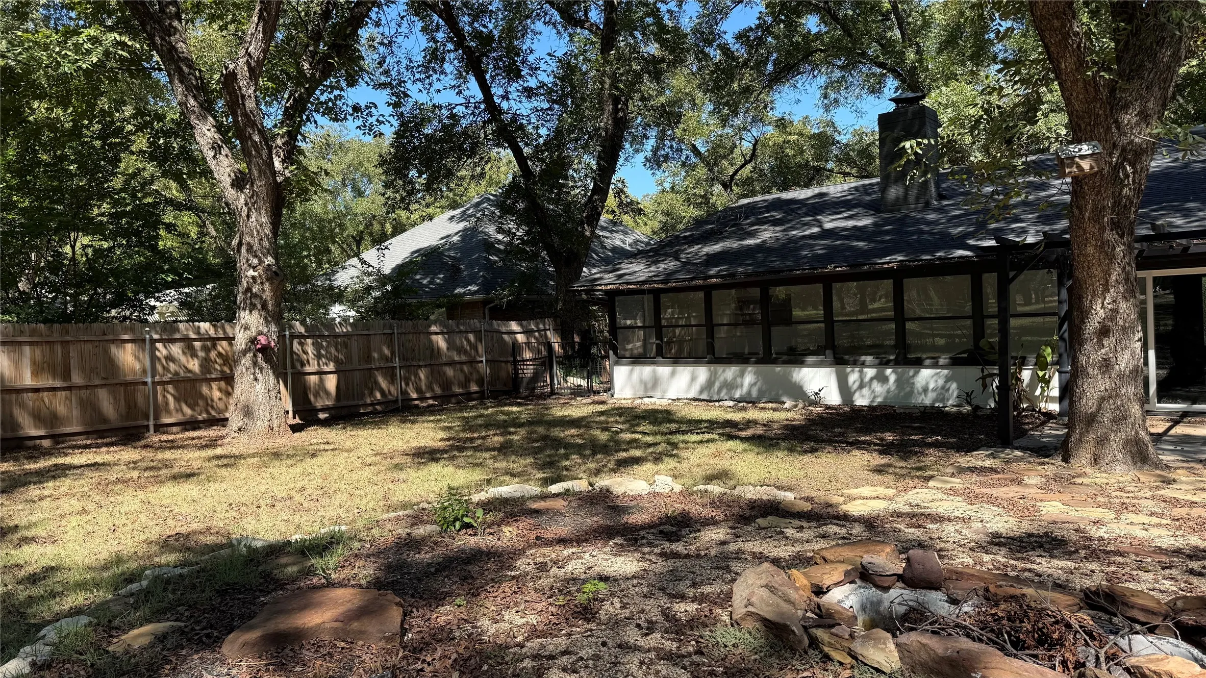 Expansive backyard featuring a wood privacy fence, mature trees, and a stone-edged fire pit area