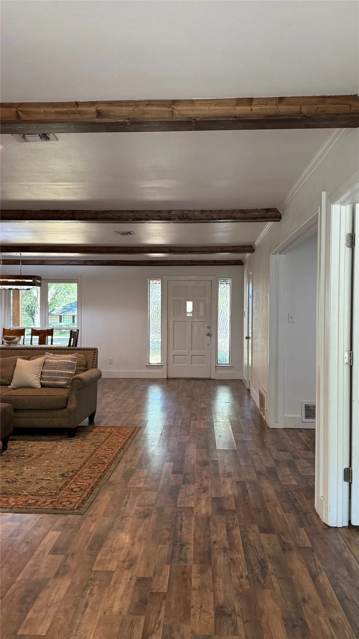 Wood-finish flooring throughout, exposed ceiling beams, white entry door with frosted glass sidelights, and white trim molding