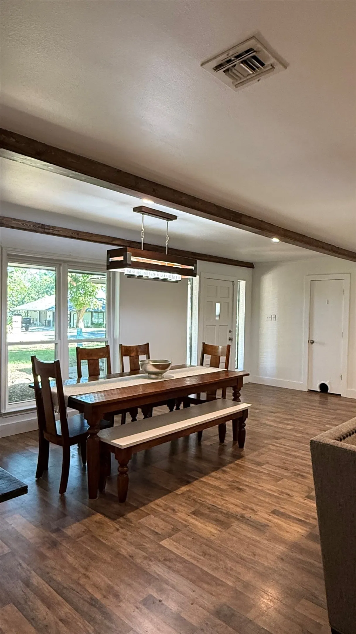 Wood-finish flooring, exposed ceiling beams, recessed lighting, and a contemporary linear chandelier illuminate this space