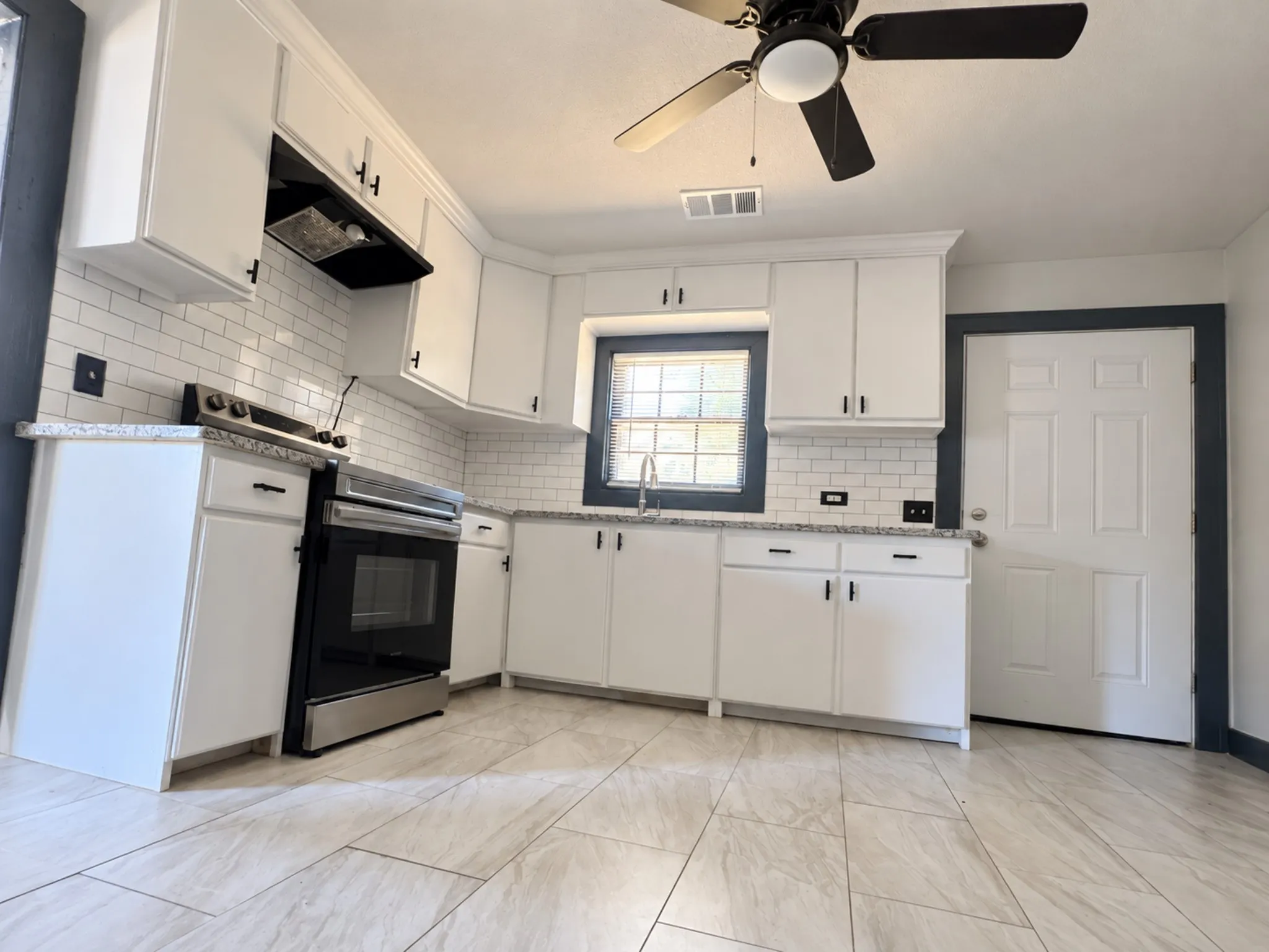 Kitchen featuring white shaker-style cabinetry, subway tile backsplash, granite-style countertops, and stainless steel appliances