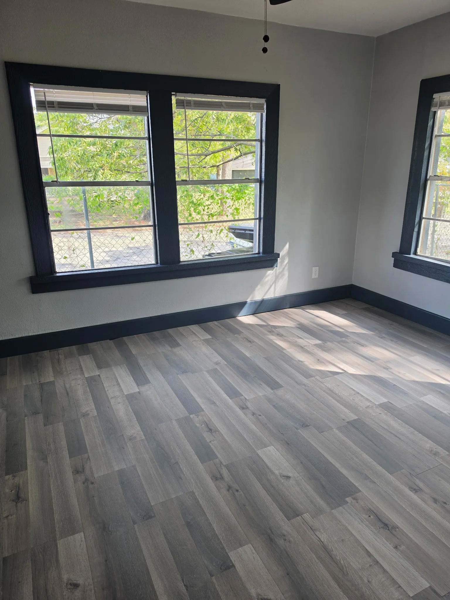 Wood-finish flooring, light gray wall paint, dark window trim, and a ceiling fan
