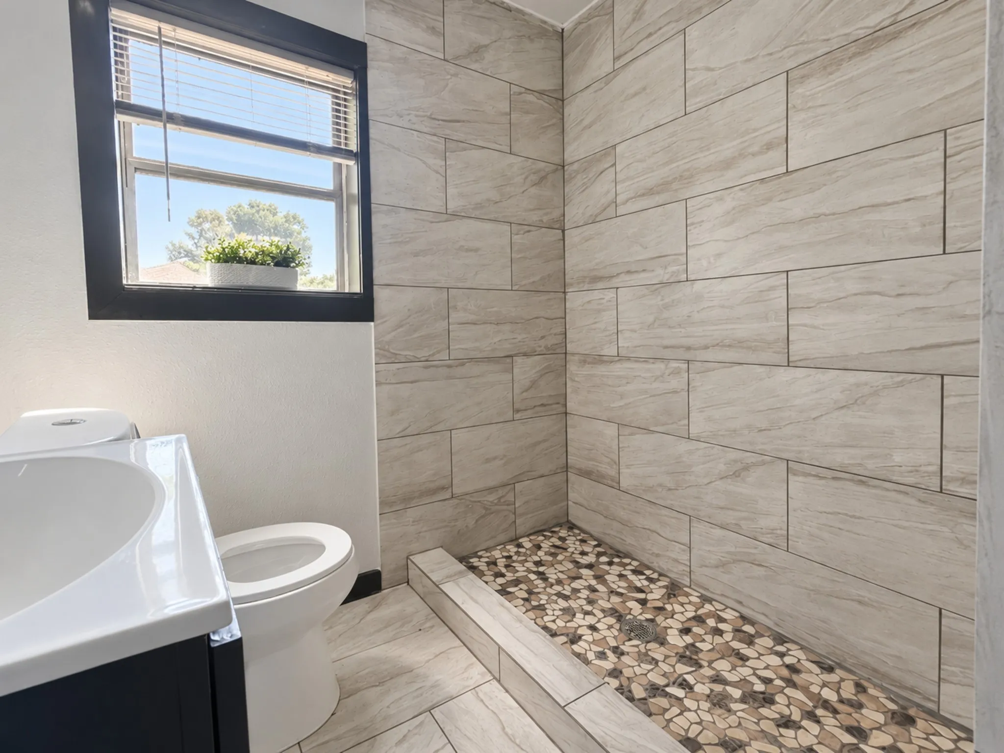 Walk-in shower with textured tile surround and pebble flooring