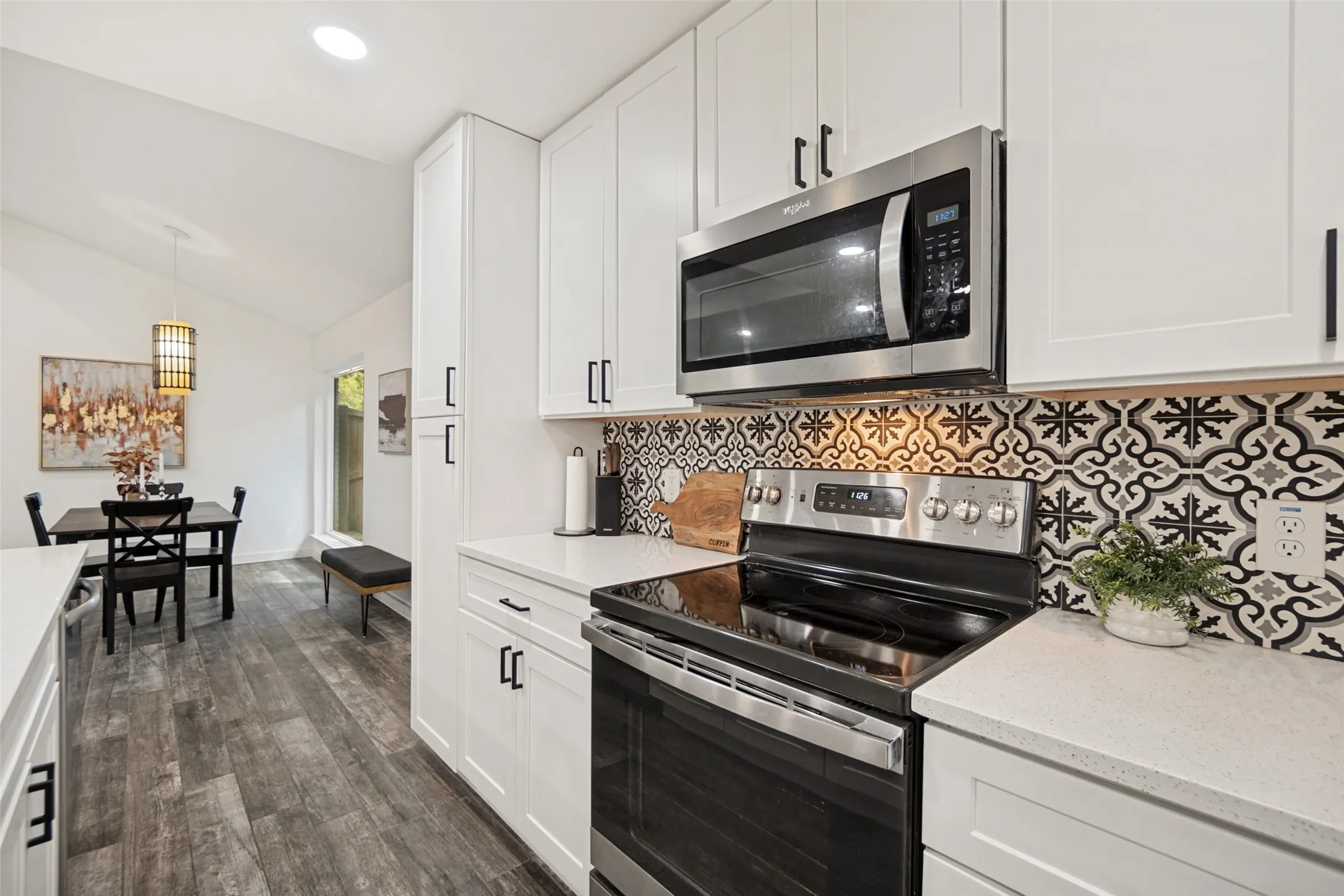 Modern kitchen featuring white shaker cabinetry, stainless steel appliances, patterned tile backsplash, and light-colored countertops