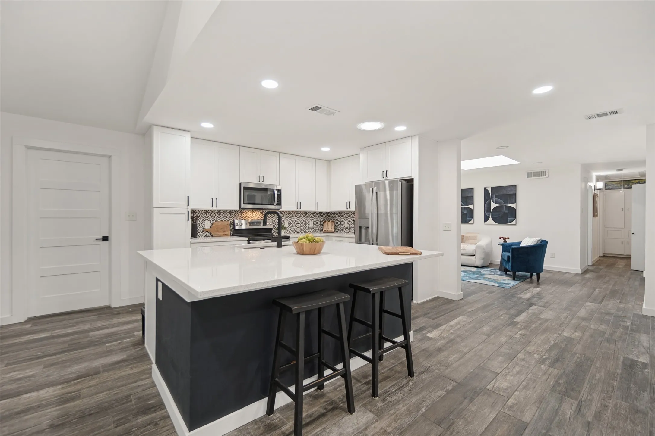 Kitchen featuring a central island with countertop seating, white cabinetry, integrated stainless steel appliances, and wood-finish flooring