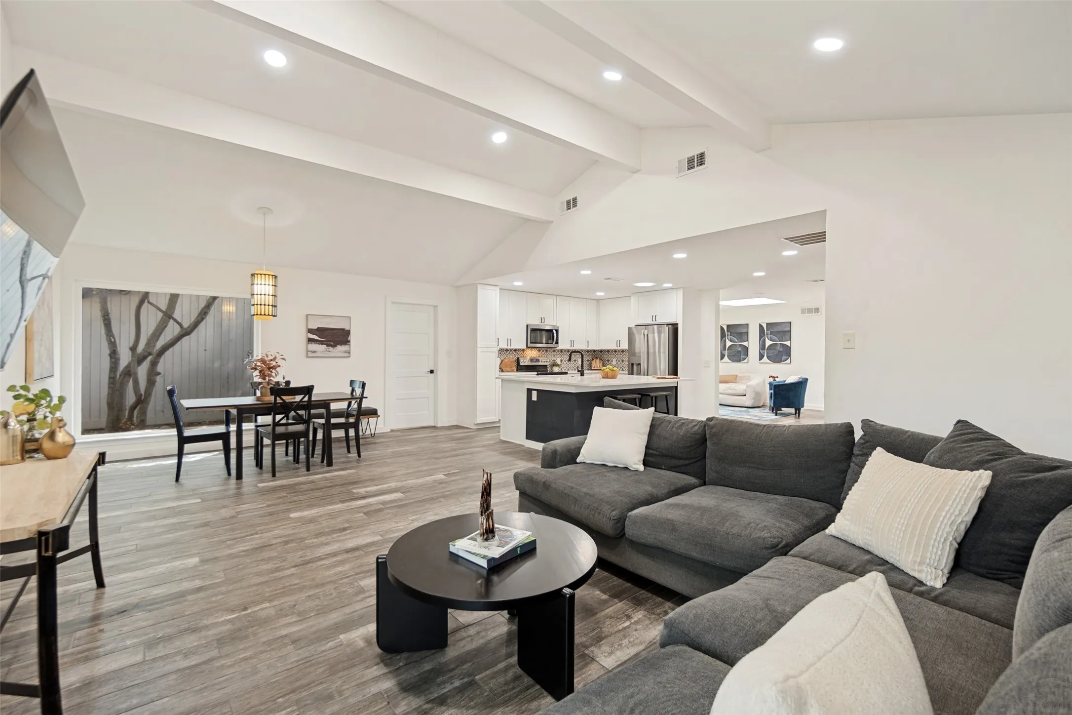 Vaulted ceiling with recessed lighting, wood-finish flooring, and a dining area with a window