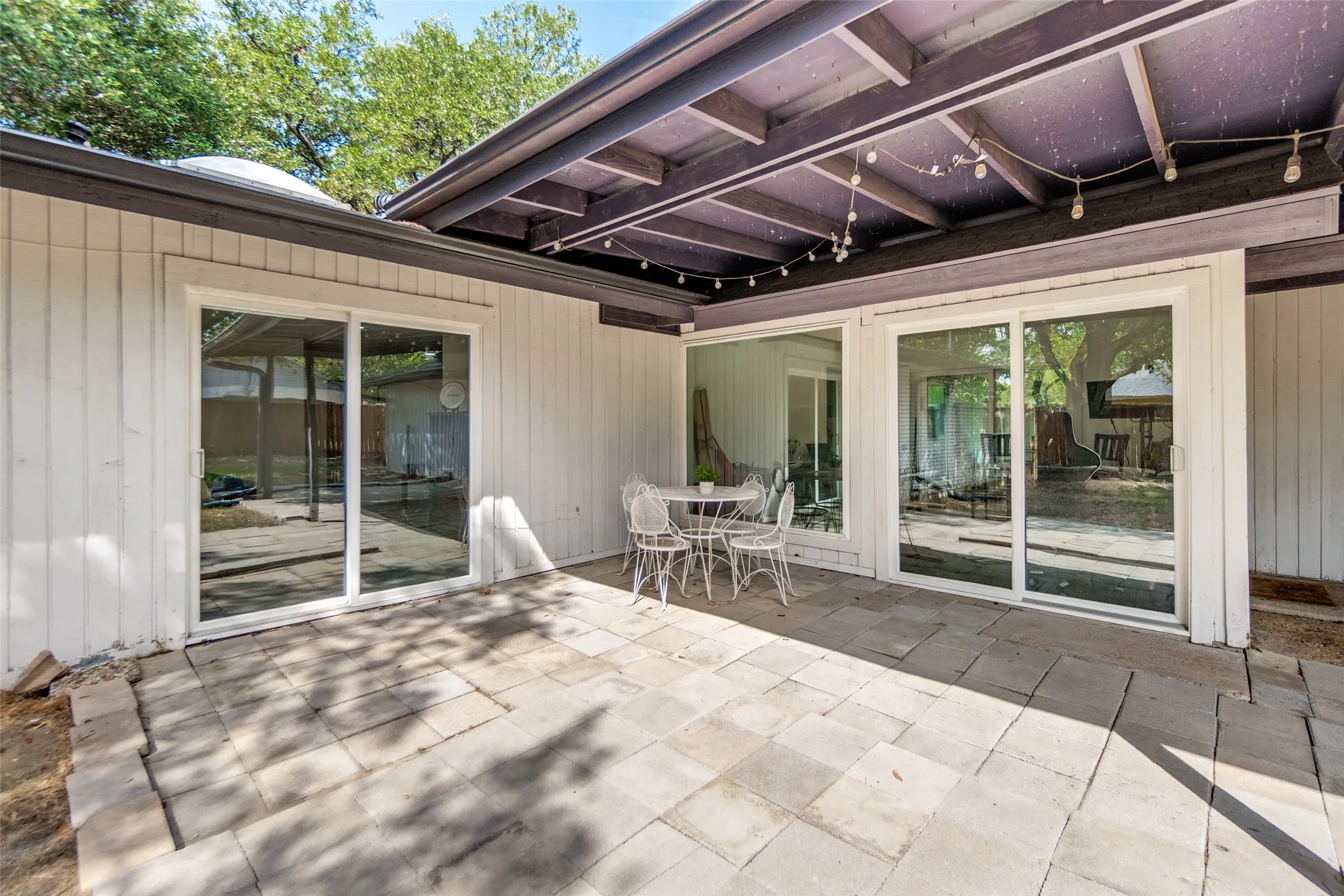 Paved patio with multiple sliding glass doors, a wood-beam overhang, and plank siding