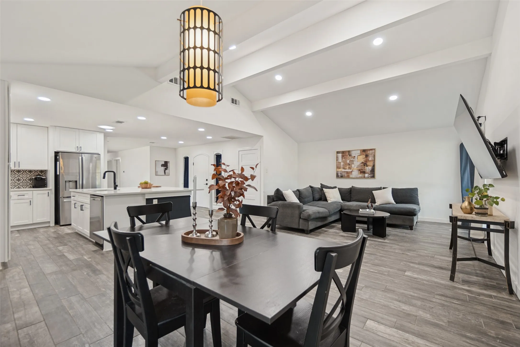 Vaulted ceilings with exposed beams, wood-finish flooring, recessed lighting, and a modern kitchen island with an undermount sink