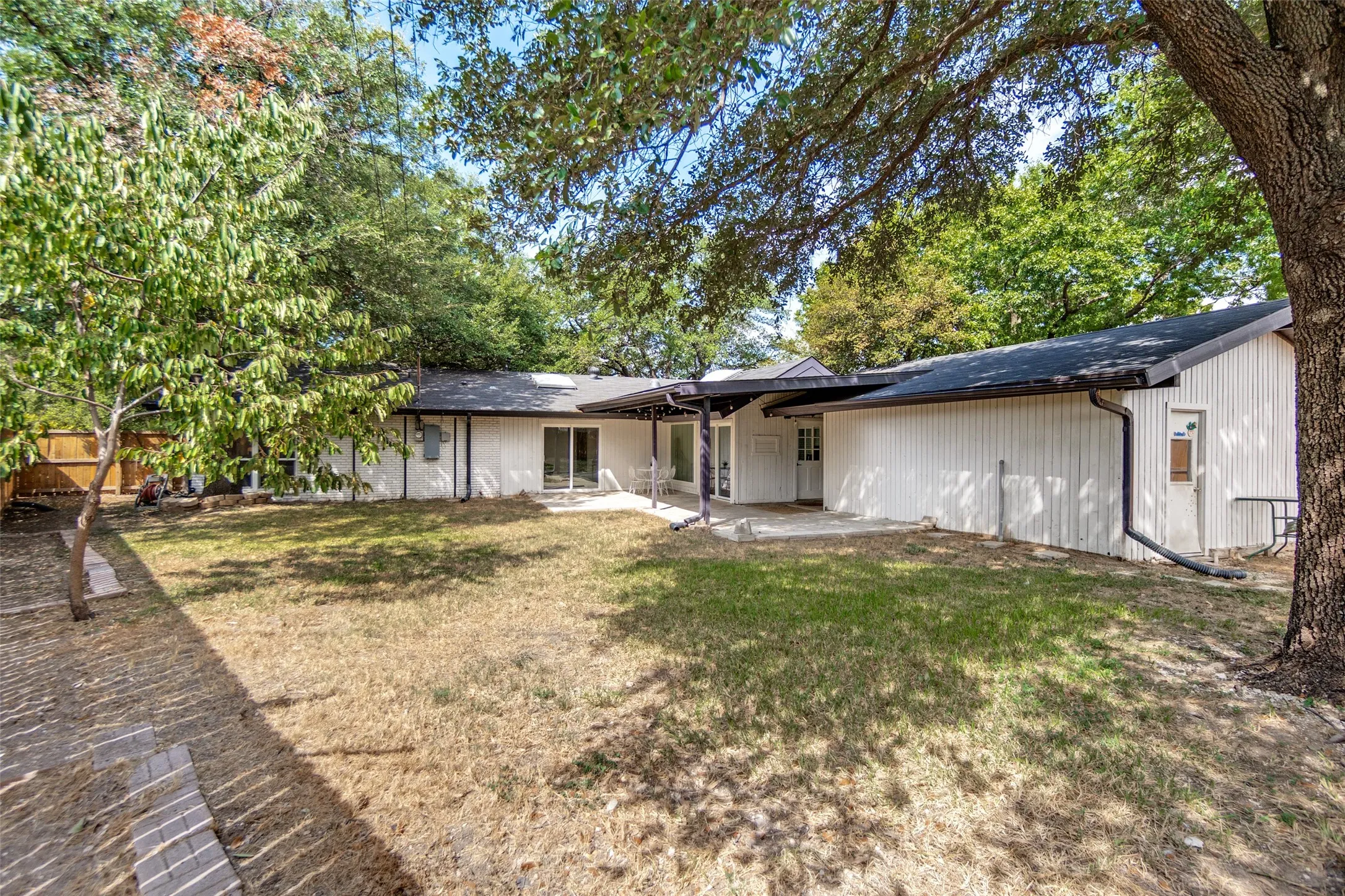 Expansive backyard with mature trees, a concrete patio, and a privacy fence