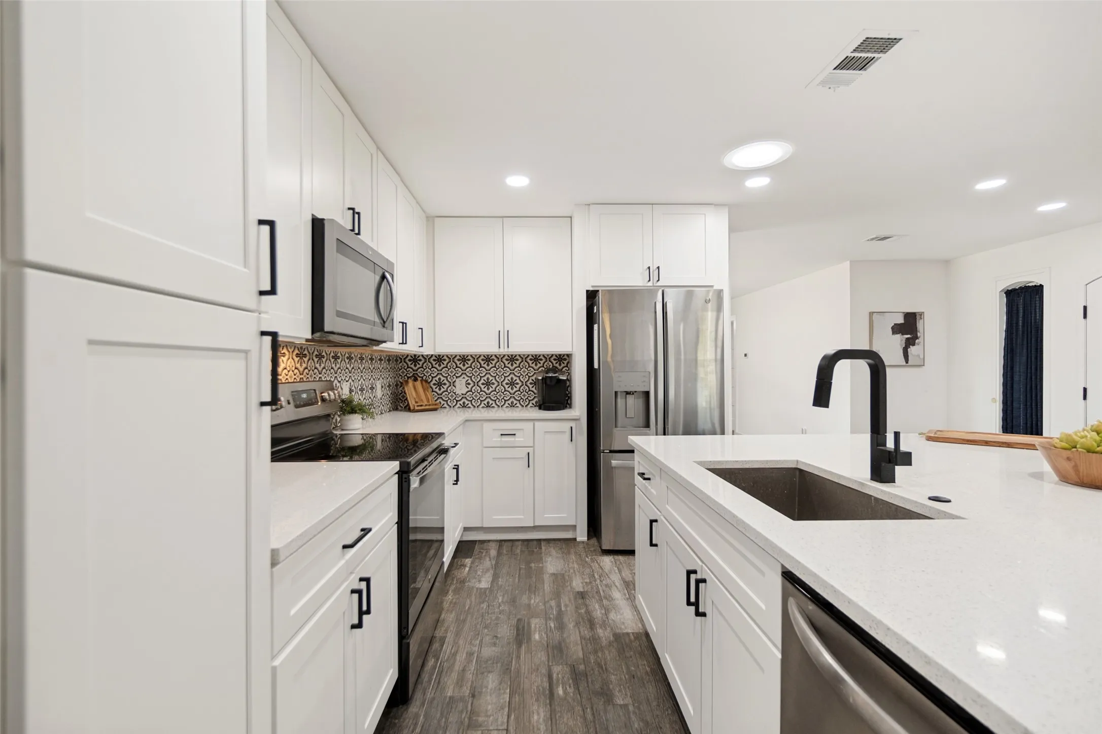 Modern kitchen featuring white shaker cabinetry, stainless steel appliances, wood-finish flooring, and a large center island with an undermount sink and matte black faucet
