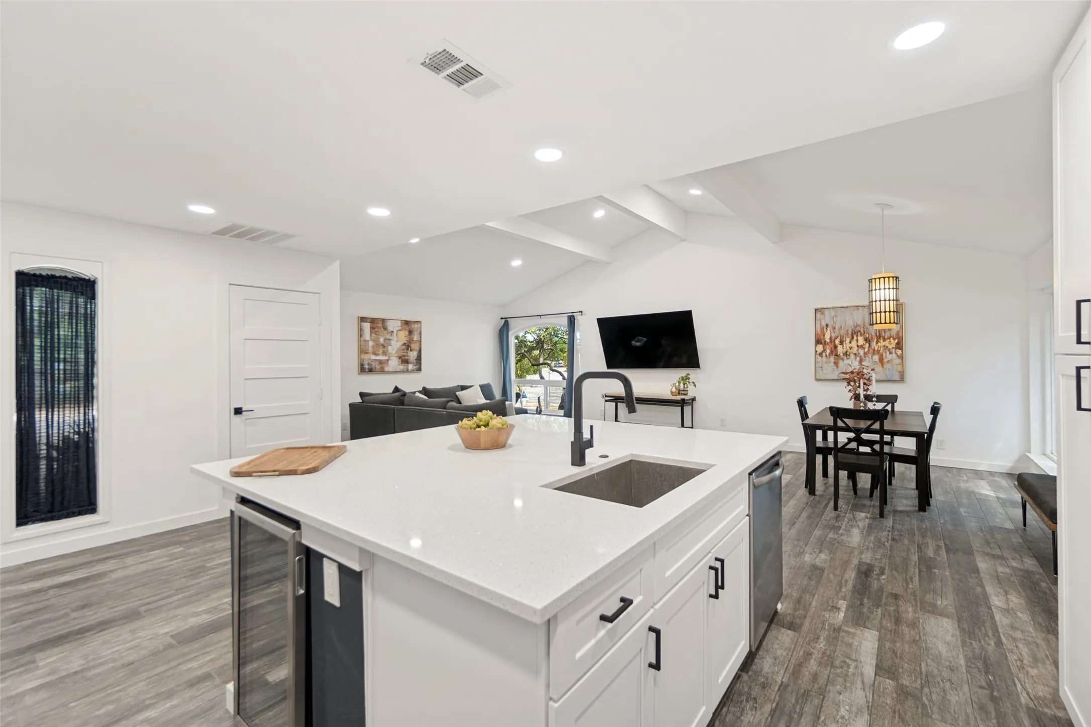 Open-concept living space with vaulted ceilings, wood-finish flooring, a kitchen island featuring a built-in beverage cooler, and recessed lighting