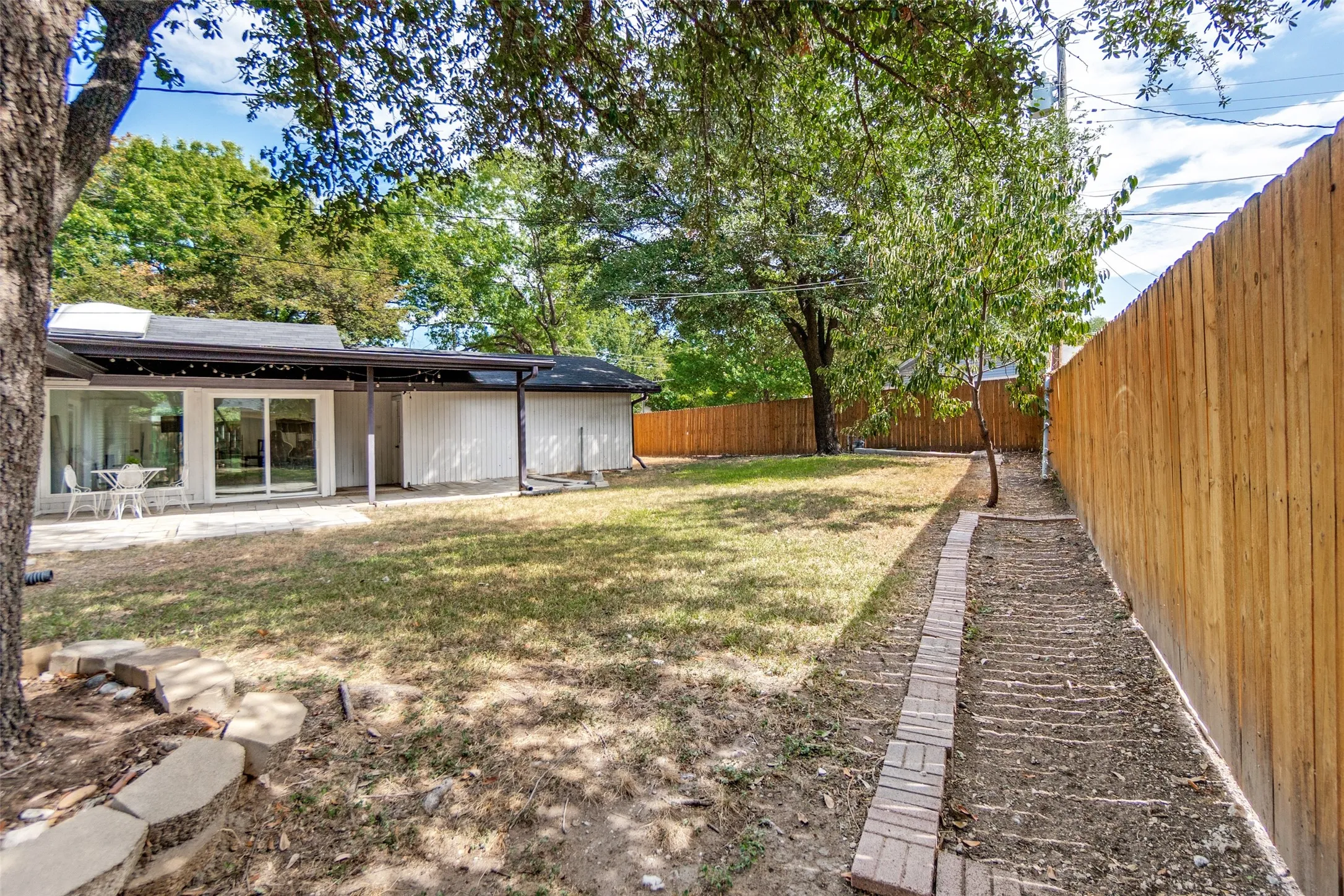 Expansive backyard featuring a privacy fence, covered patio, and large sliding glass doors