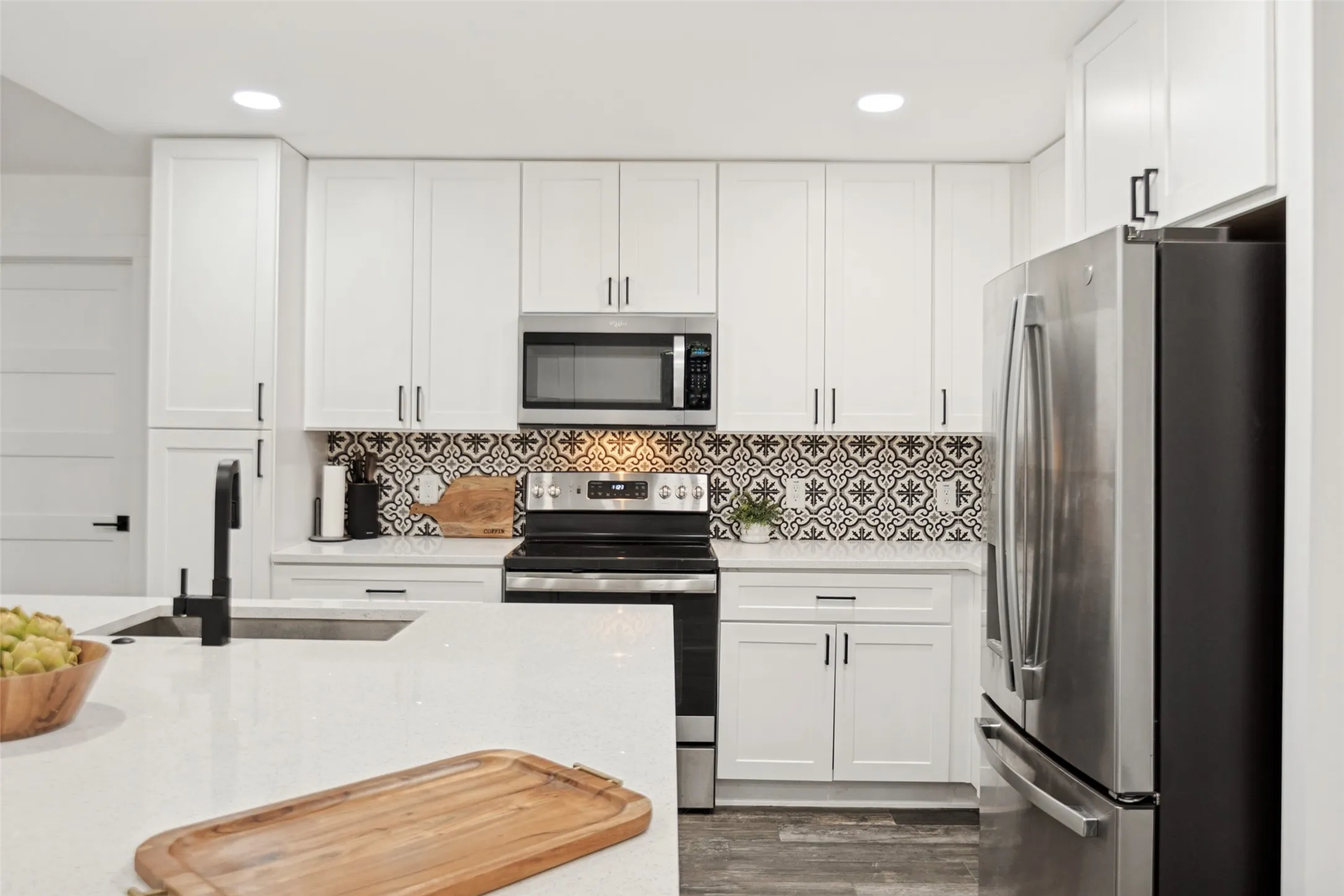 White shaker cabinetry, patterned tile backsplash, stainless steel appliances, white countertops, and wood-finish flooring