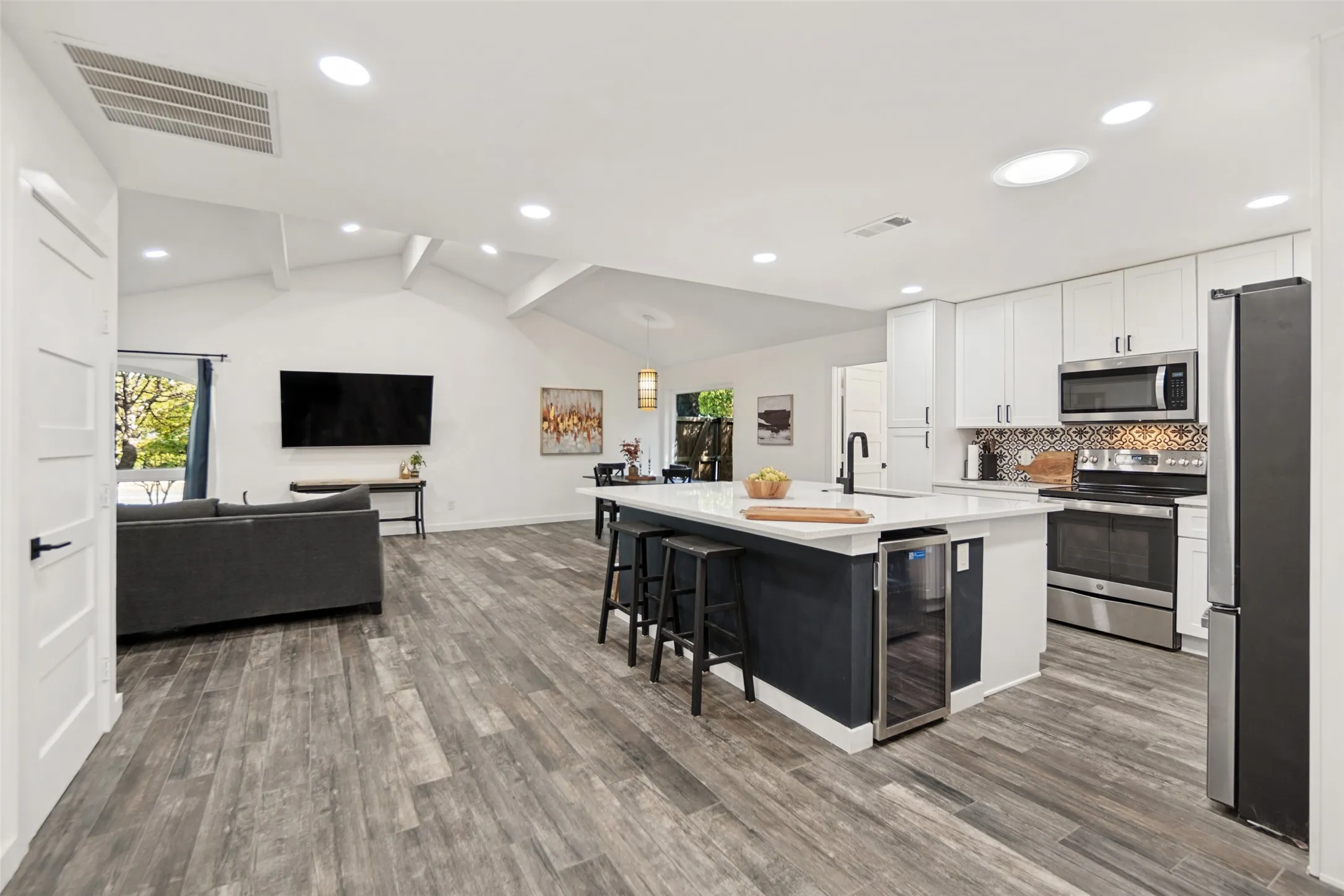 Vaulted ceilings, wood-finish flooring, white cabinetry, stainless steel appliances, and a kitchen island with built-in beverage refrigerator