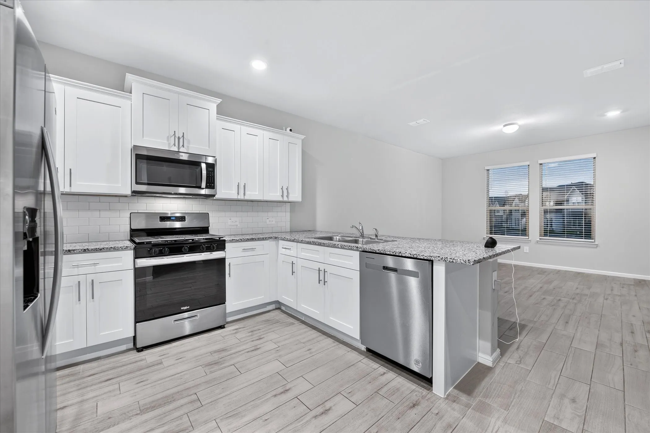 Kitchen featuring white cabinetry, stainless steel appliances, speckled countertops, a white subway tile backsplash, and wood-finish flooring
