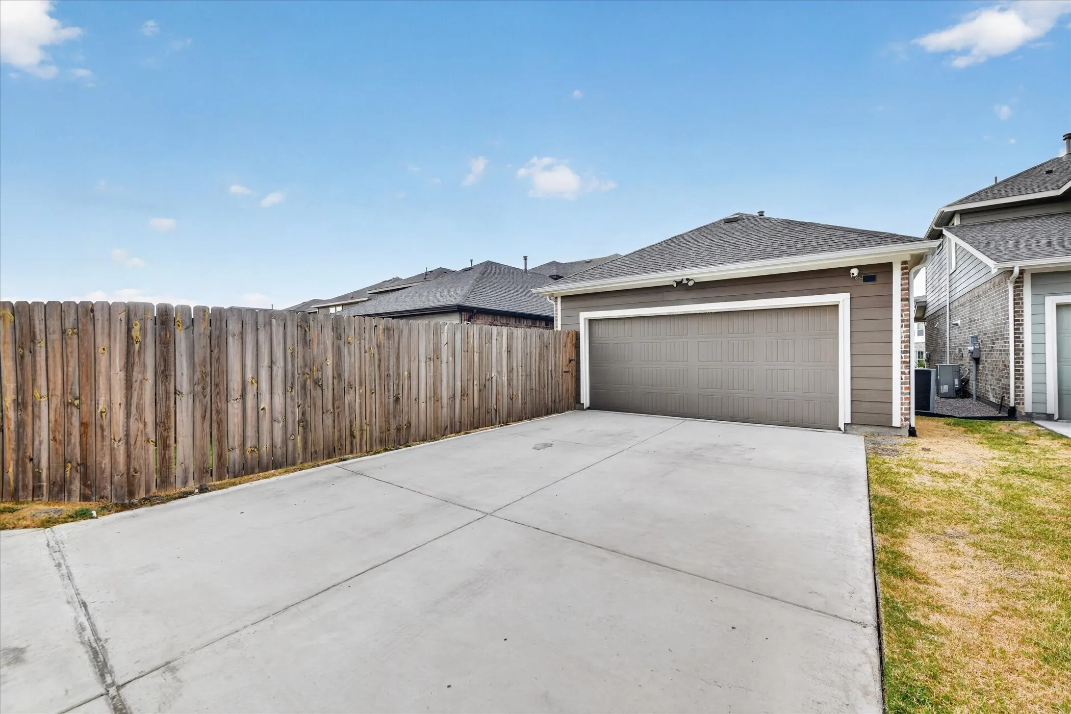 Concrete driveway with a wood fence and a garage featuring a gray door