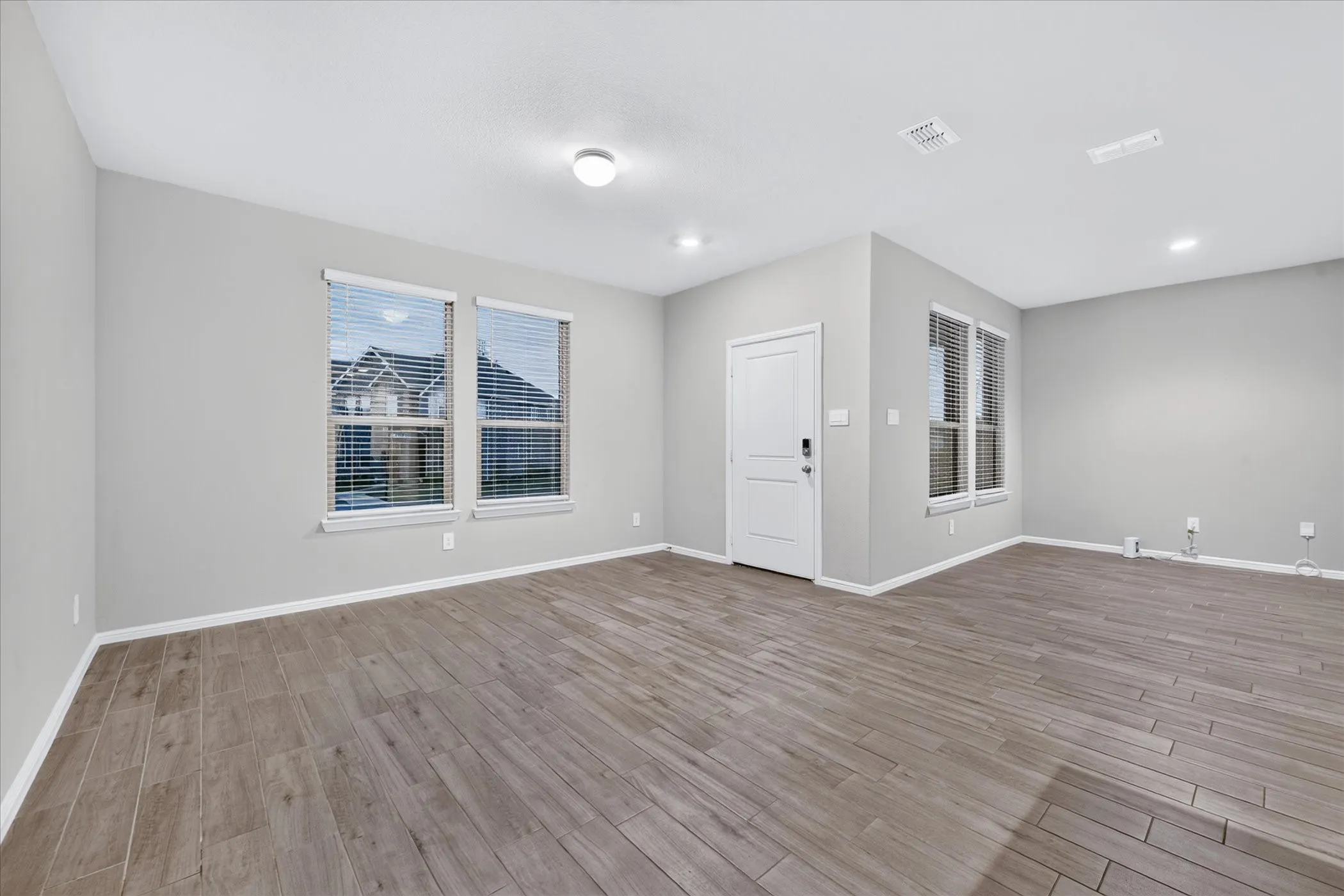 Wood-finish tile flooring throughout, multiple windows with blinds, white trim, recessed lighting, and a solid white door