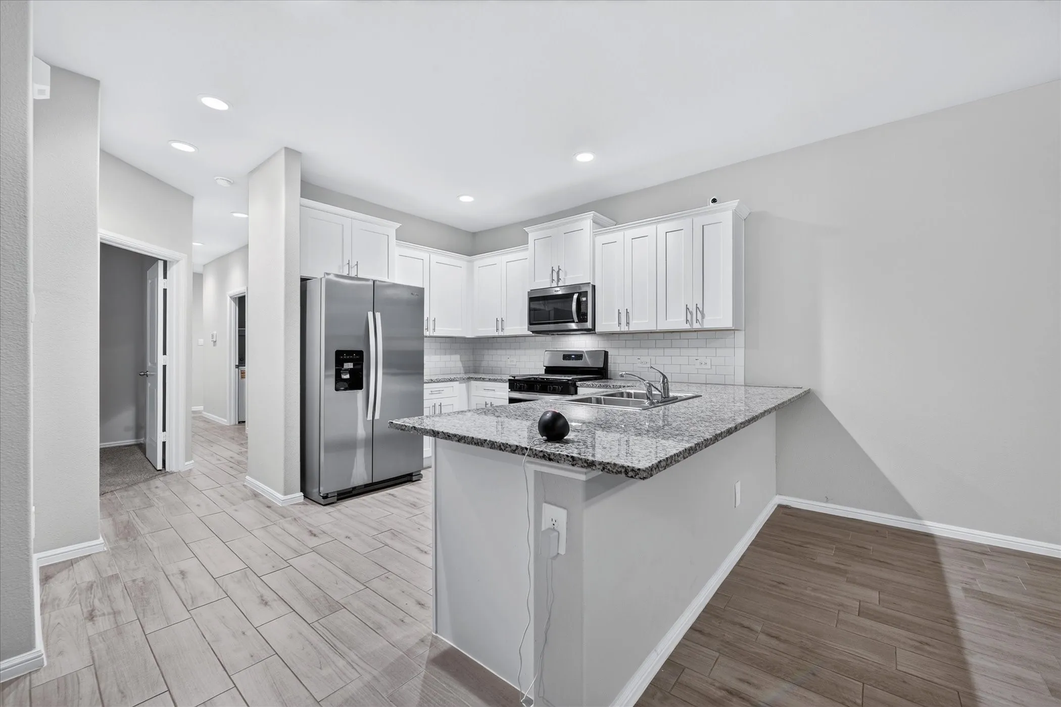Kitchen with white shaker cabinetry, stainless steel appliances, speckled stone countertops, and wood-finish flooring