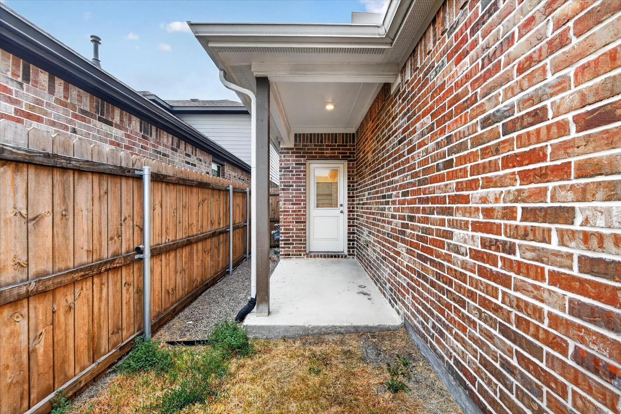 Brick exterior with a covered concrete patio, recessed lighting, and a white door with transom window