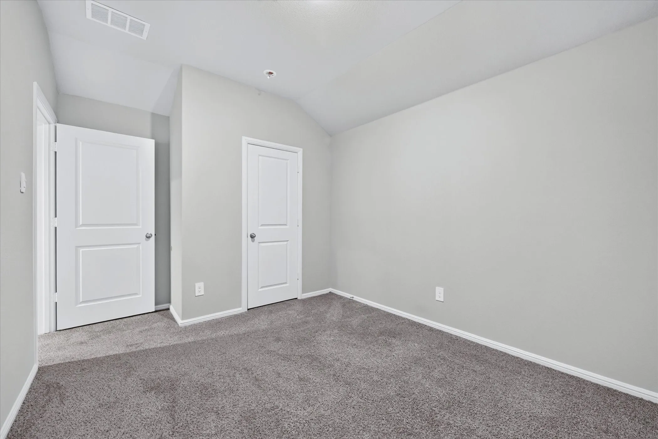 Carpeted flooring, vaulted ceiling, white trim throughout, and two panel doors