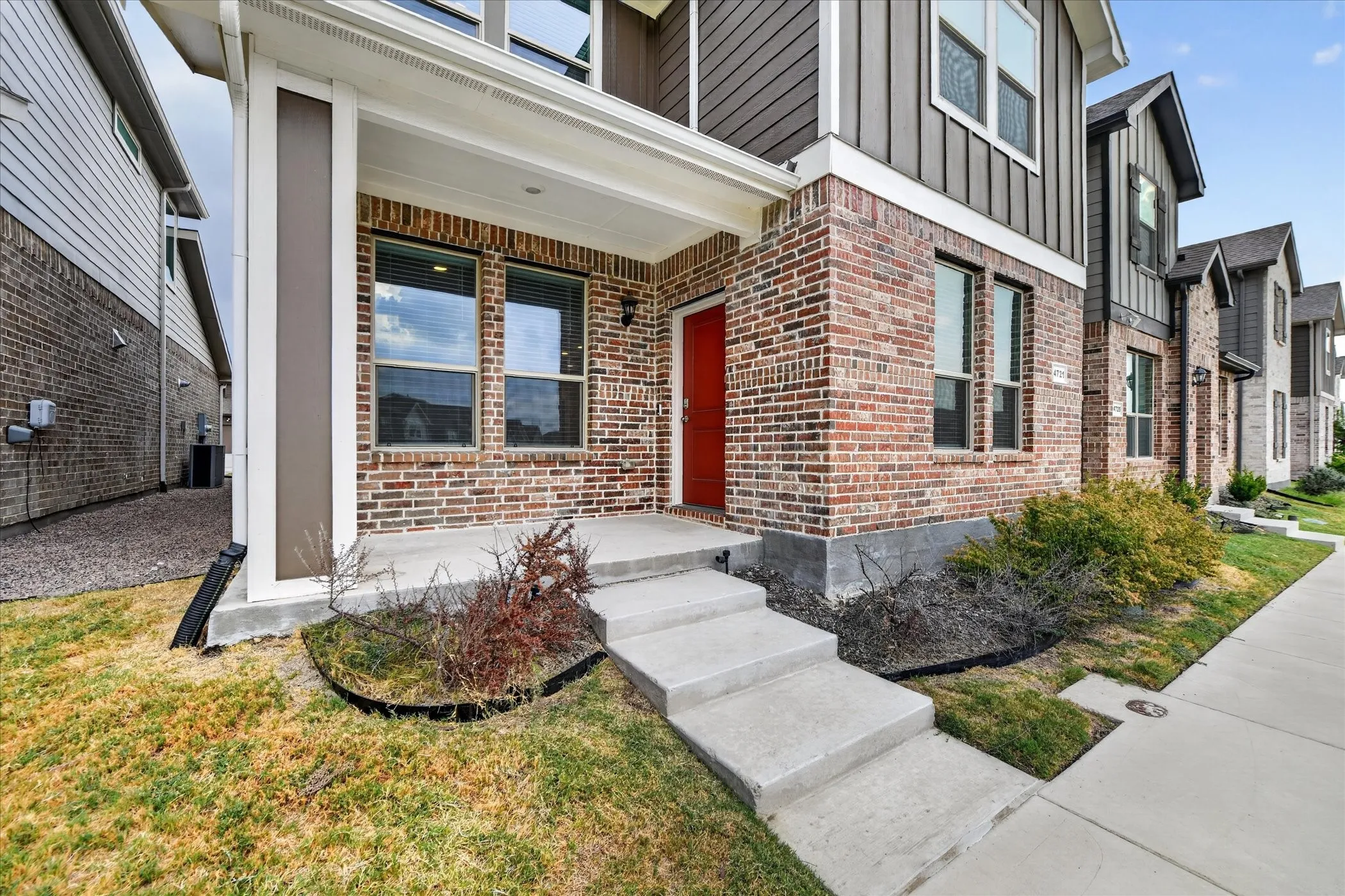 Brick and vertical siding exterior with a covered porch, concrete steps, and an accent-color entry door