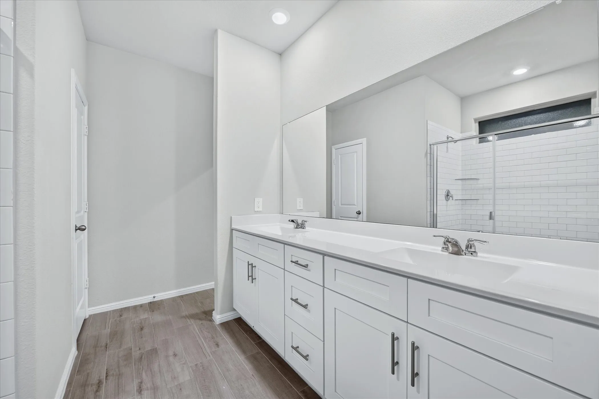 Dual vanity with white cabinetry and integrated sinks, wood-finish flooring, and a walk-in shower with subway tile