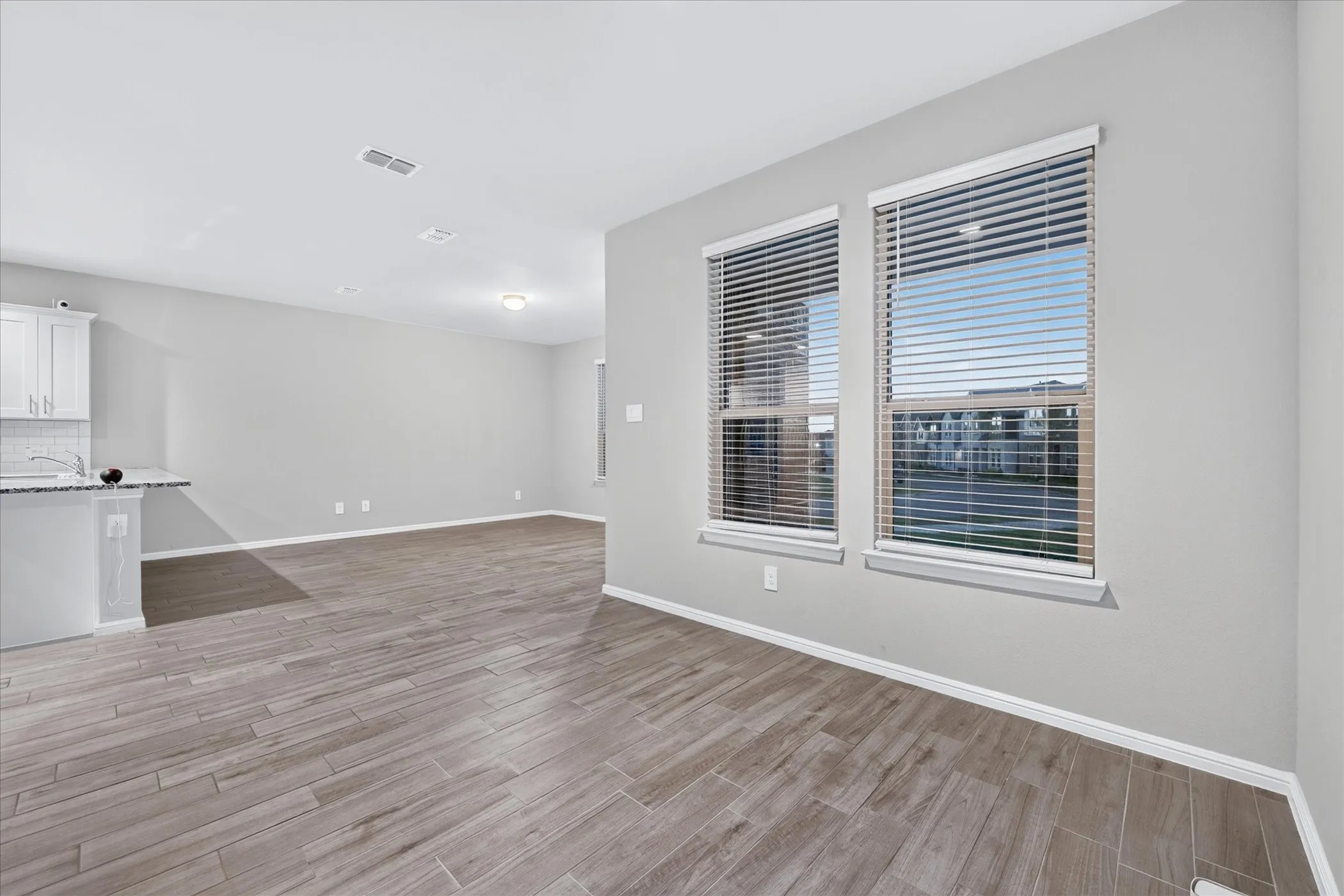 Bright interior with wood-finish flooring, two large windows, white cabinetry, and a textured backsplash