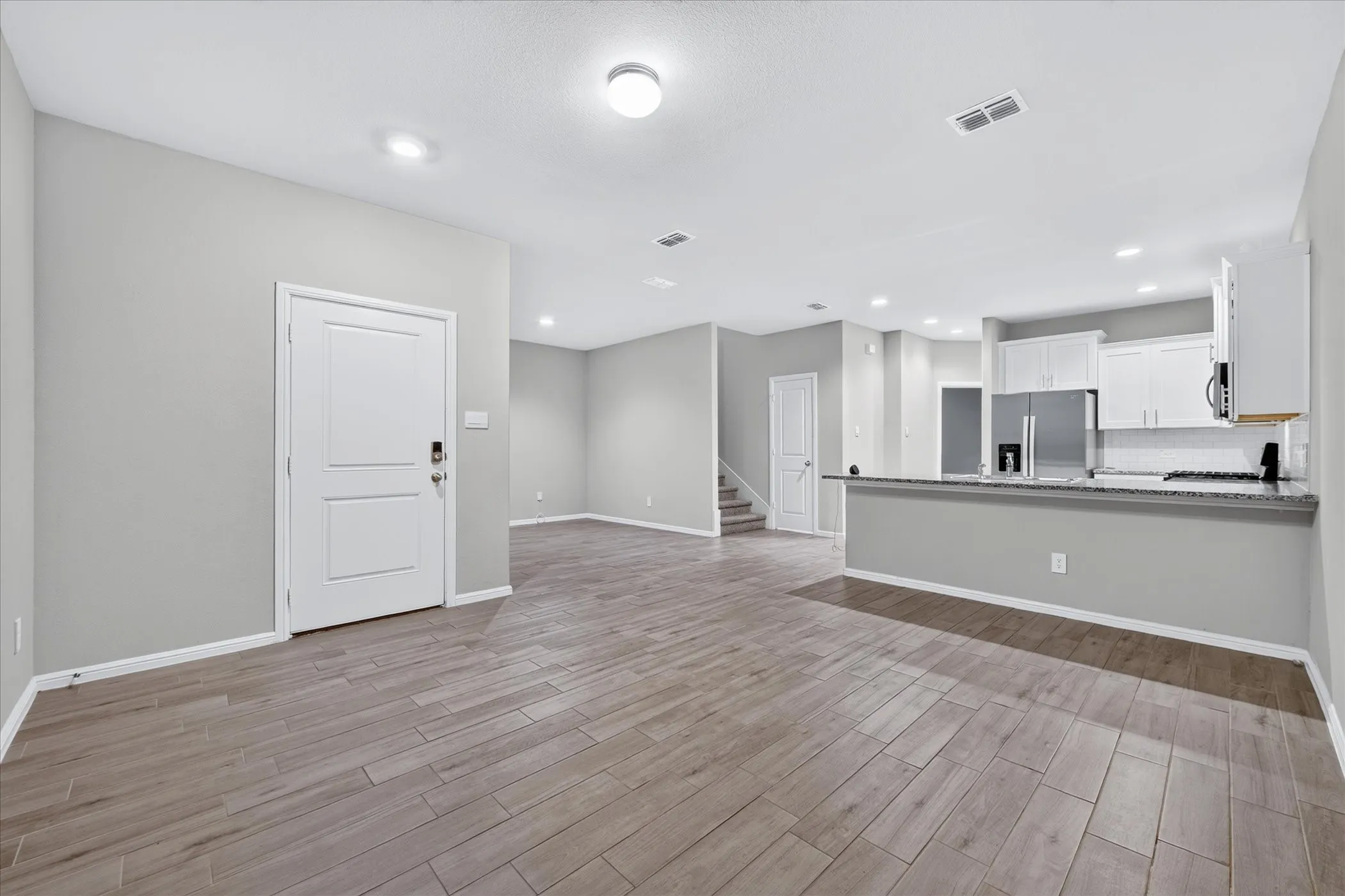 Expansive room featuring wood-finish flooring, recessed lighting, and a white paneled door
