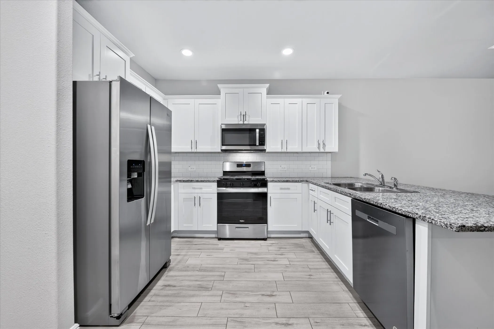 Kitchen featuring white cabinetry, stainless steel appliances, speckled stone countertops, a tile backsplash, and wood-finish flooring