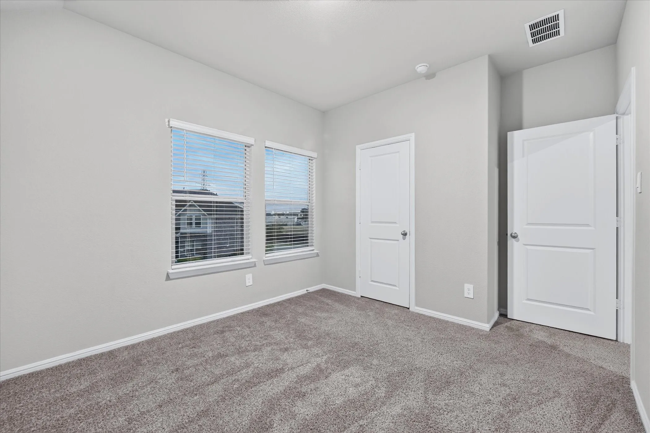 Two paneled interior doors, dual windows with blinds, gray plush carpeting, and light gray wall paint