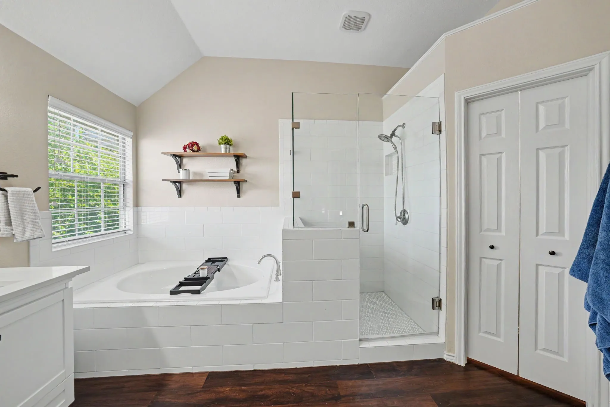 Spacious bathroom featuring a built-in soaking tub, a glass-enclosed shower with white subway tile, and wood-finish flooring