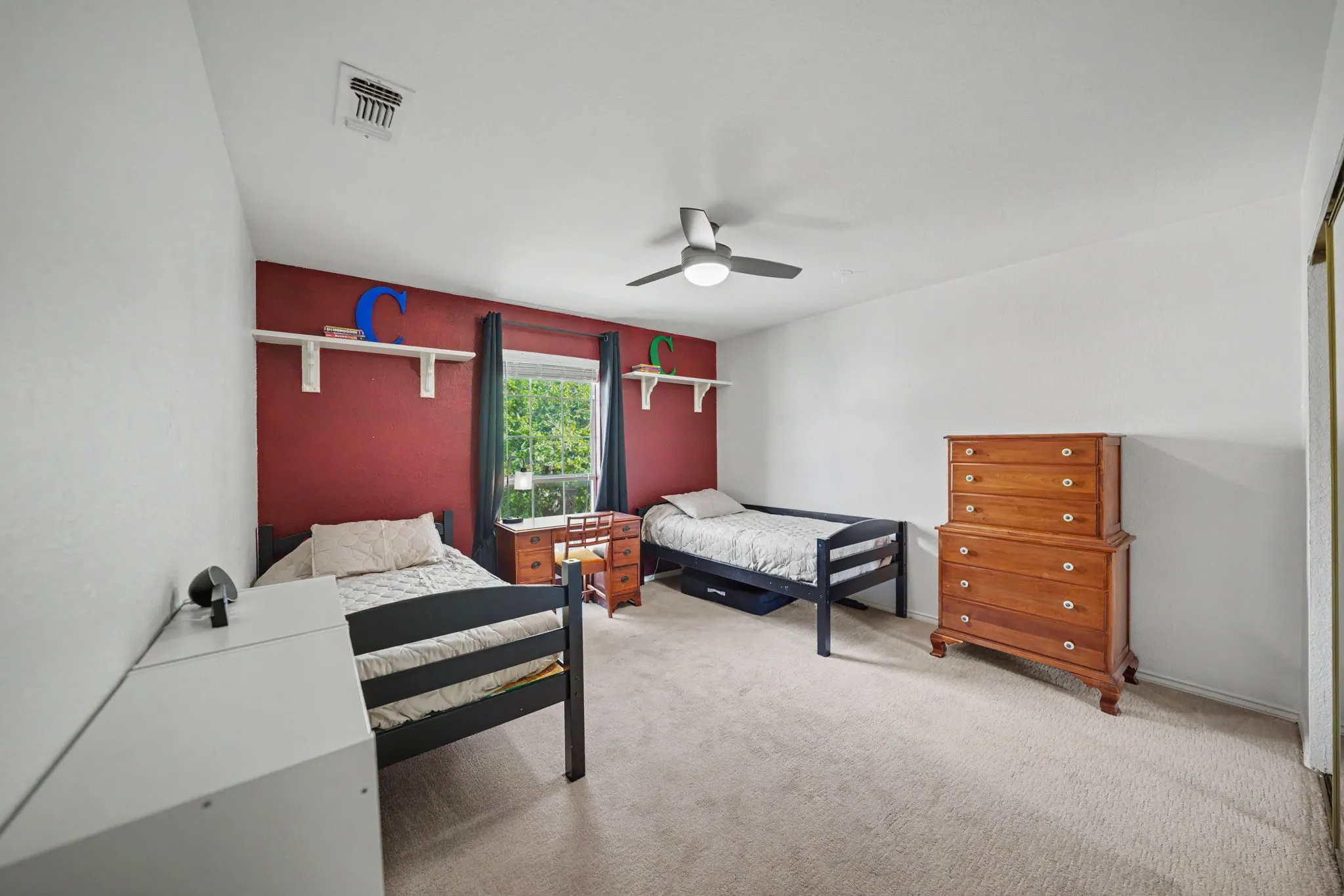 Plush carpet flooring, a ceiling fan with integrated lighting, a window with curtains, and built-in shelving