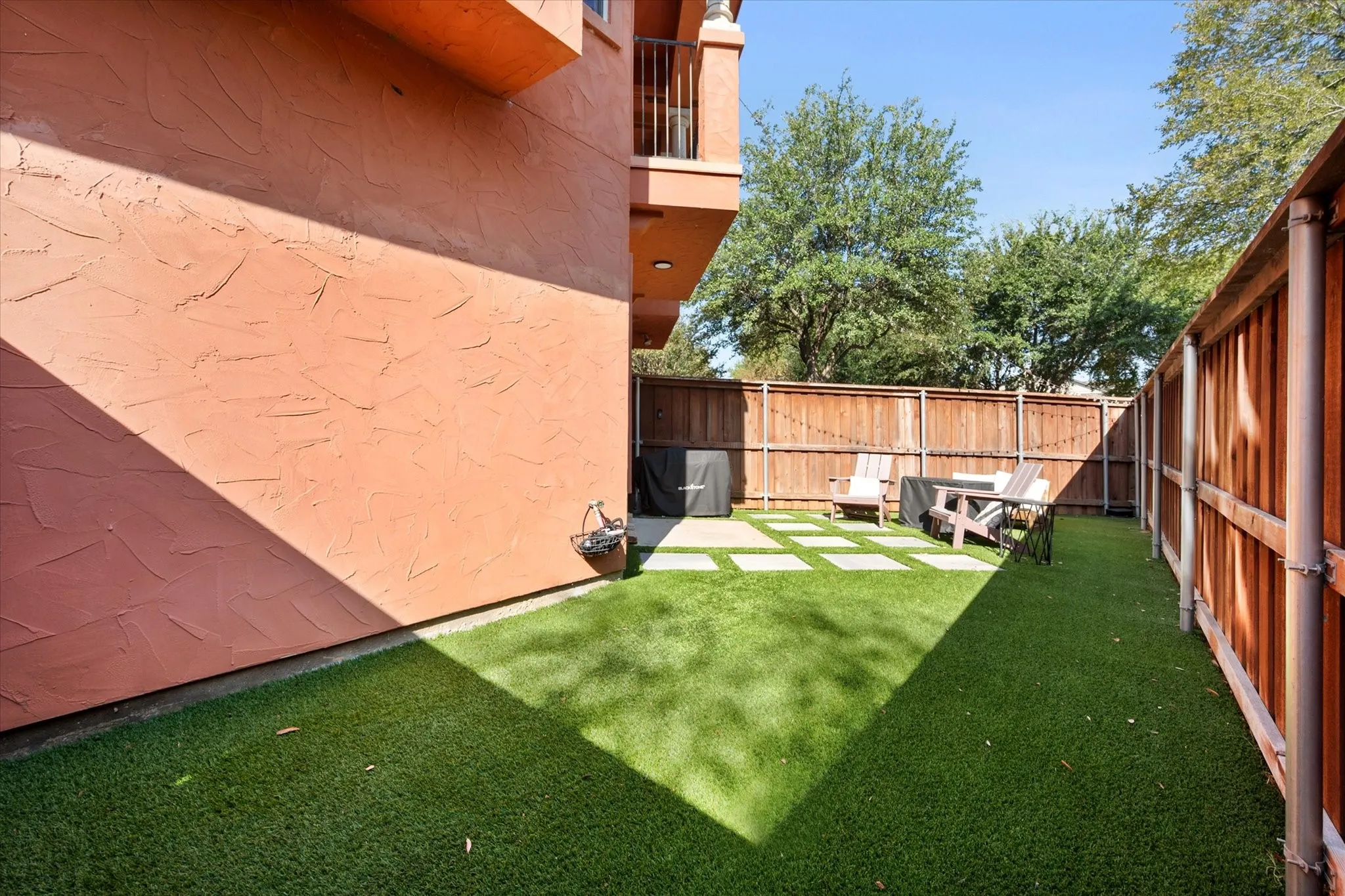 Private outdoor area featuring artificial turf, concrete stepping stones, and wood fencing