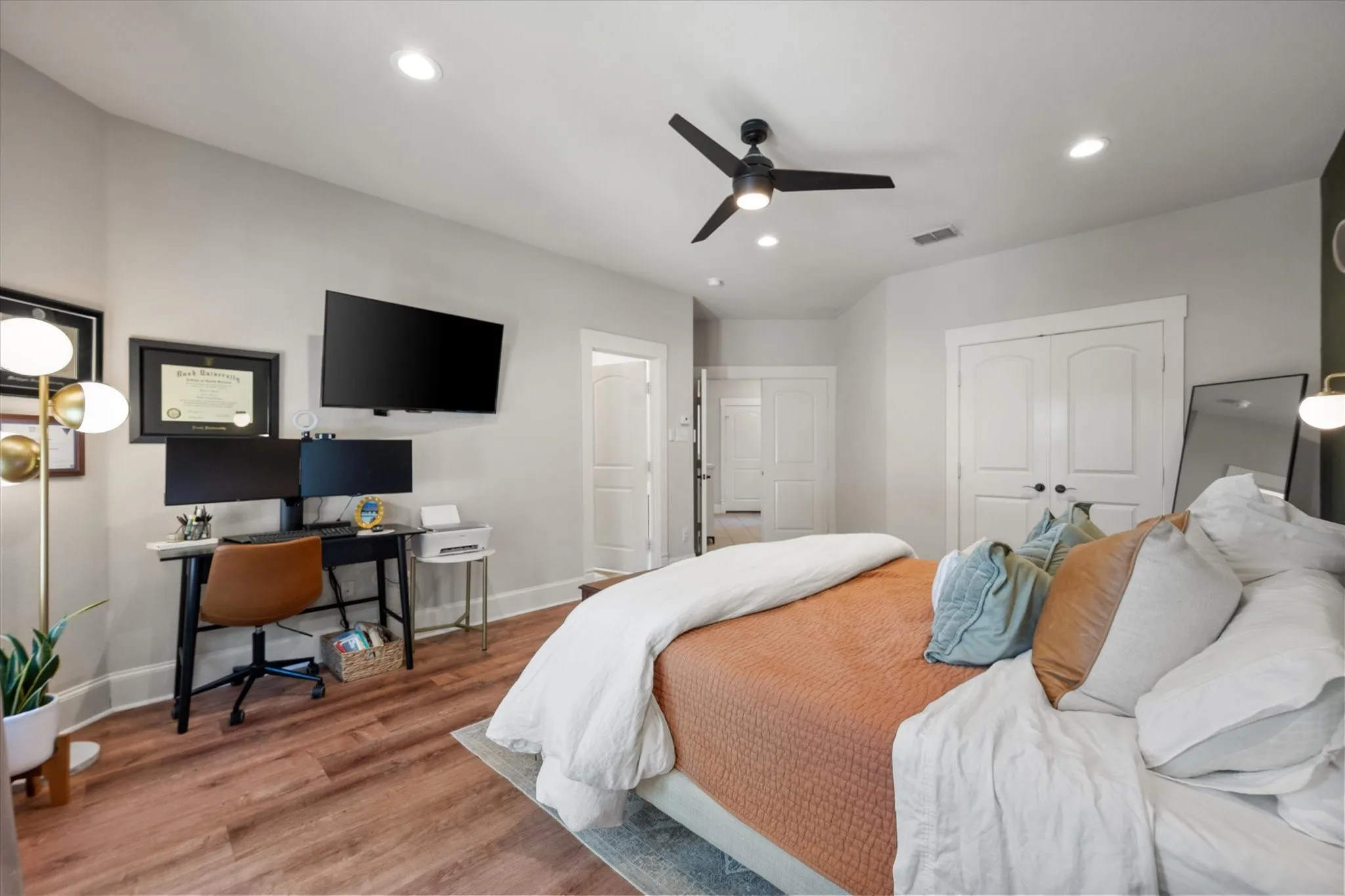 Spacious Primary Bedroom featuring neutral paint, LVP wood like flooring, recessed lighting, modern light + ceiling fan fixture, and views of the paneled doors leading to the Ensuite Bathroom, Entryway, and Closet