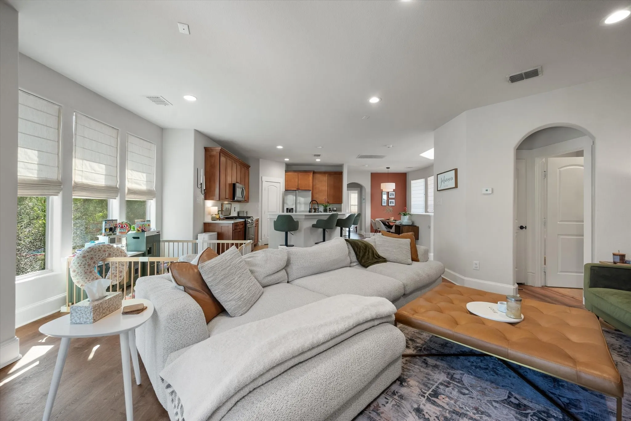 Open-concept Living space featuring neutral paint, LVP wood like flooring, recessed lighting, arched doorways leading to secondary bedrooms and bathrooms, and multiple windows with custom window treatments