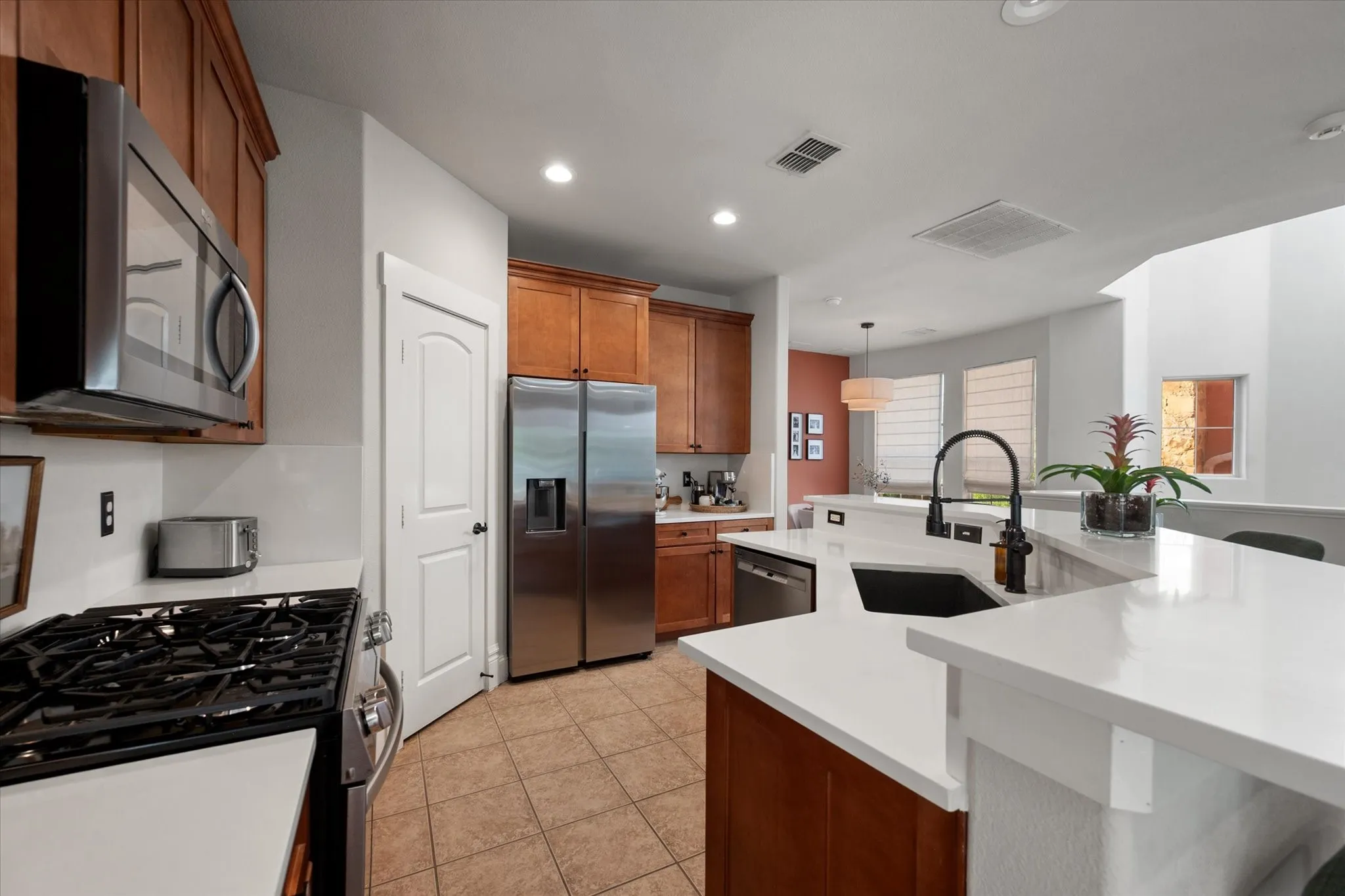 Stainless steel appliances, wood cabinetry, white countertops, tile flooring, and a black gooseneck faucet