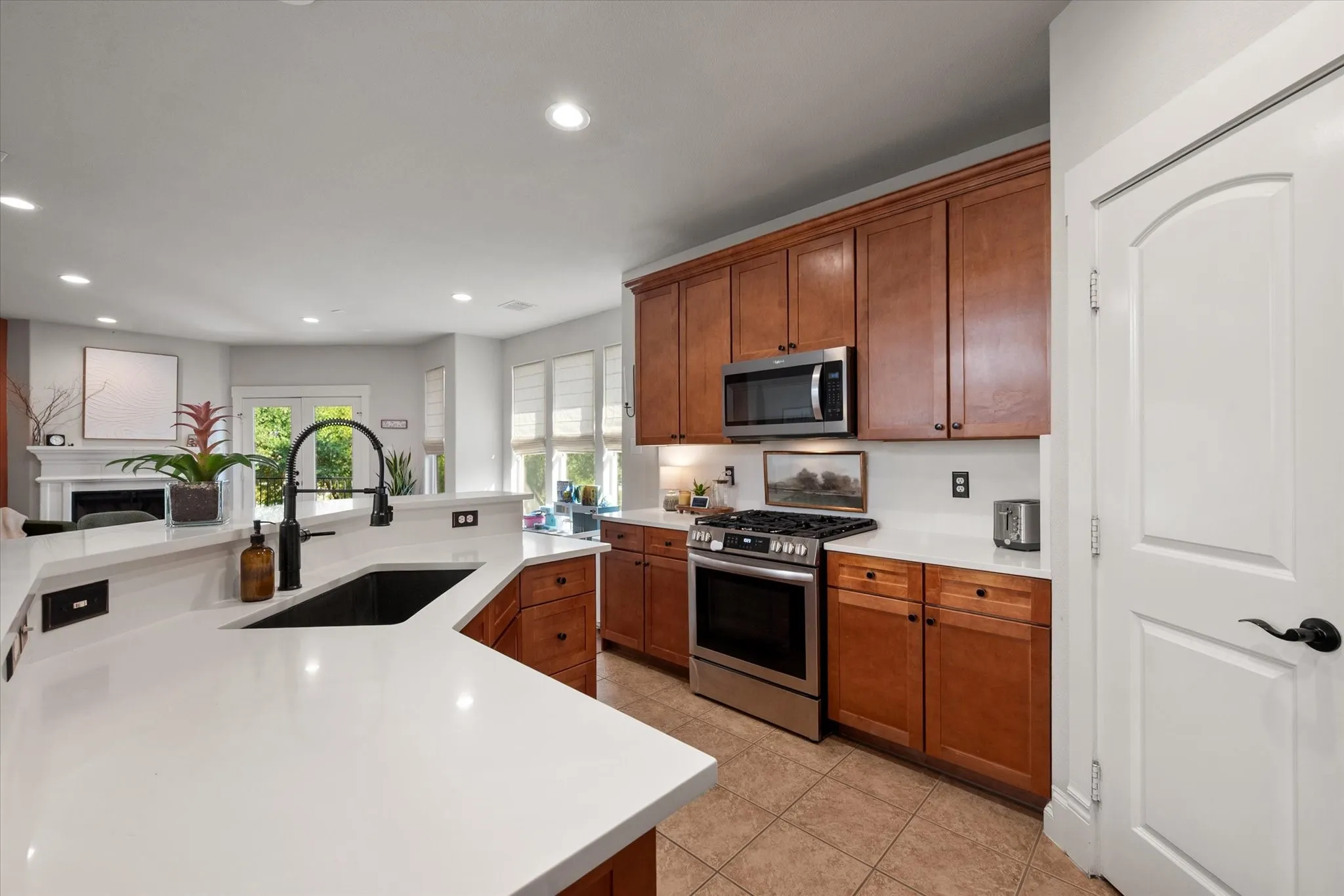 Kitchen featuring neutral paint, white quartz countertops, stainless steel appliances, wood cabinetry, recessed lighting, a pantry, and tile flooring overlooking the open-concept living and dining areas