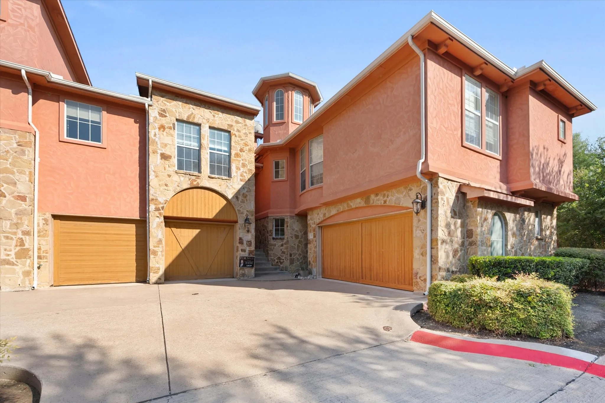 Stucco exterior with stone accents, arched garage doors, multiple windows, and a turret architectural feature