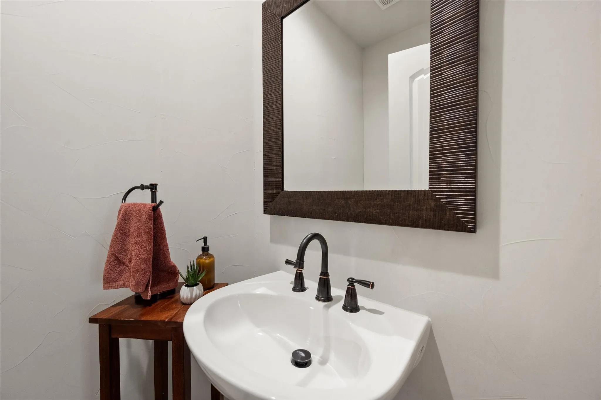 Wall-mounted pedestal sink with bronze-finish faucet, framed mirror, and textured wall finish