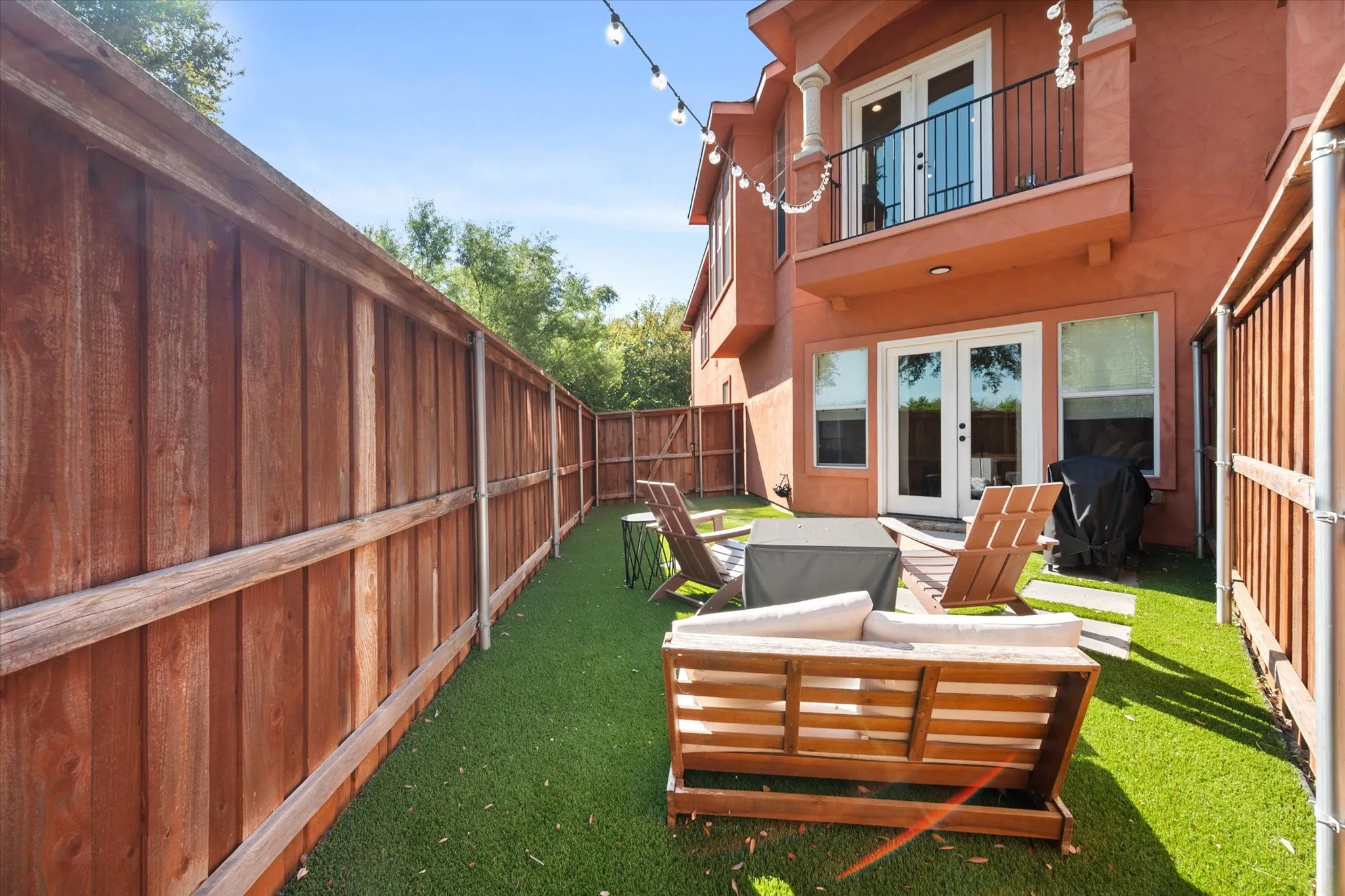 Private fenced yard with artificial turf, a stucco exterior, and a second-story balcony