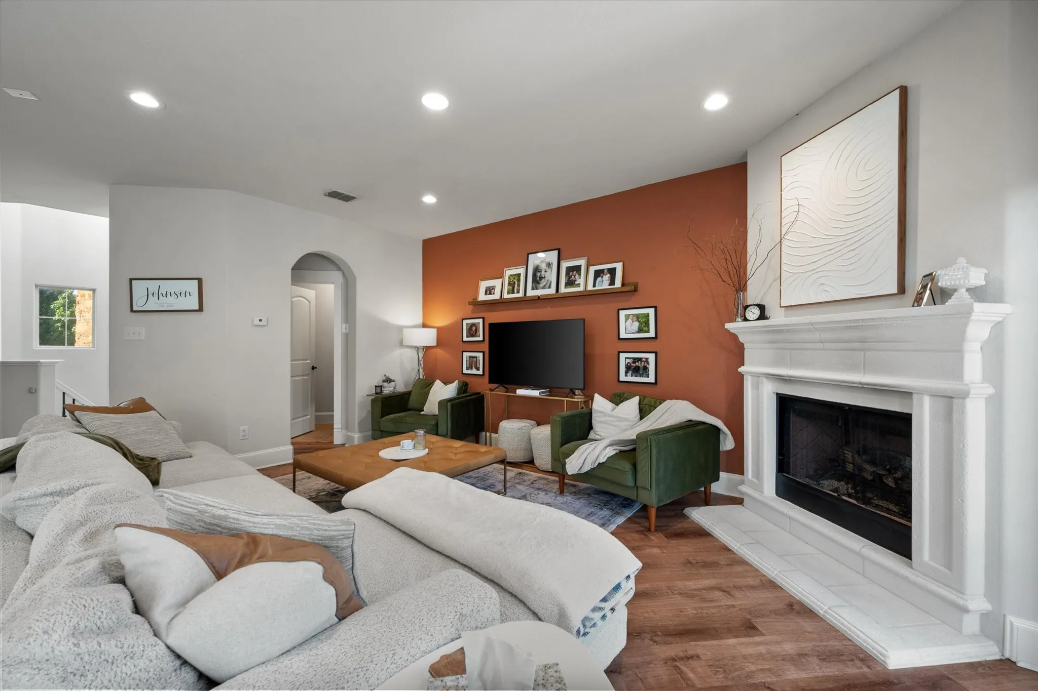 Open concept Living Area featuring LVP wood like flooring, a fireplace with white mantel, recessed lighting, and arched doorway leading to a half bathroom