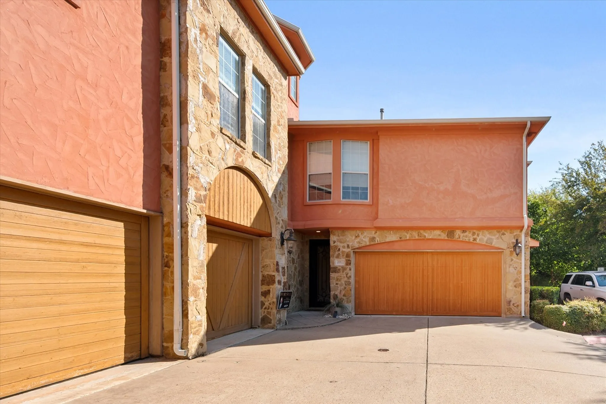 View from the paved driveway of the front door and two car garage, featuring stucco and stone exterior