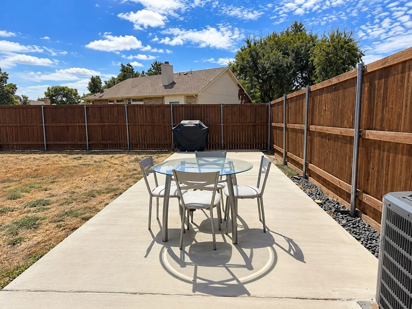 Expansive backyard featuring a concrete patio, wood privacy fencing, and stone landscape edging