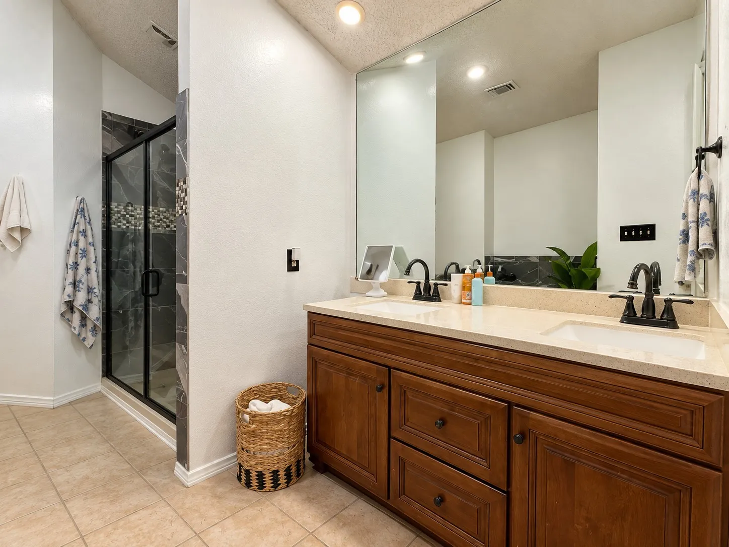 Dual sink vanity with wood-finish cabinetry, light-toned countertop, and tile flooring